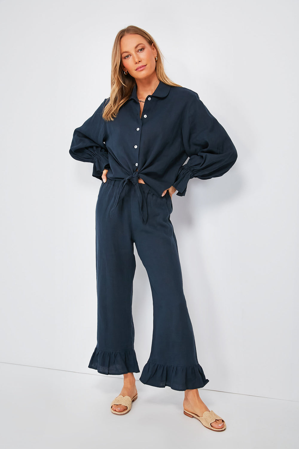 Woman in a Sleeper navy rumba set with button-up long-sleeve shirt featuring ruffle cuffs and matching ruffled pants, paired with light-colored slip-on sandals.