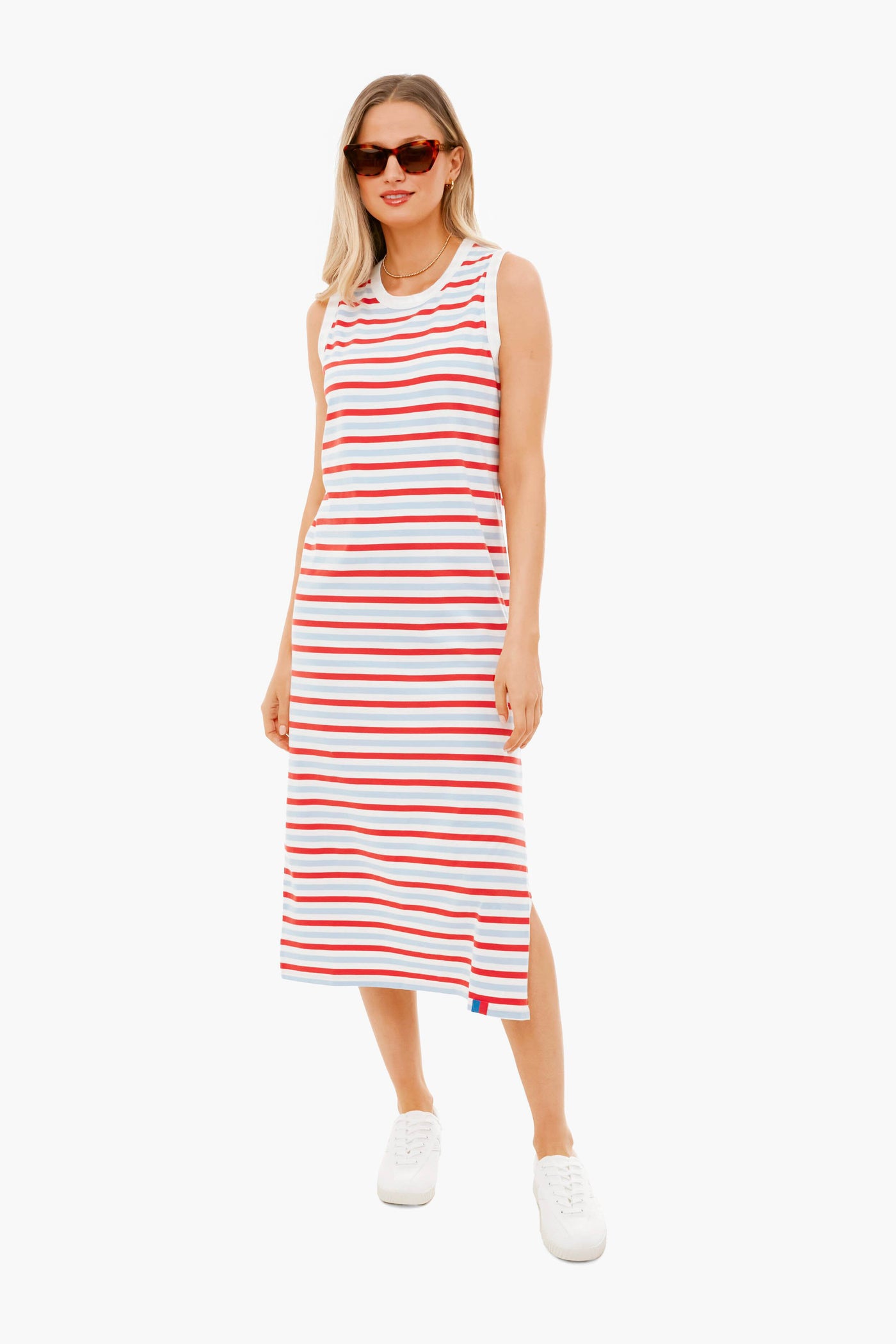 A woman wears a KULE sleeveless midi tank dress with horizontal red, white, and blue stripes in 100% cotton, styled with white sneakers and sunglasses.
