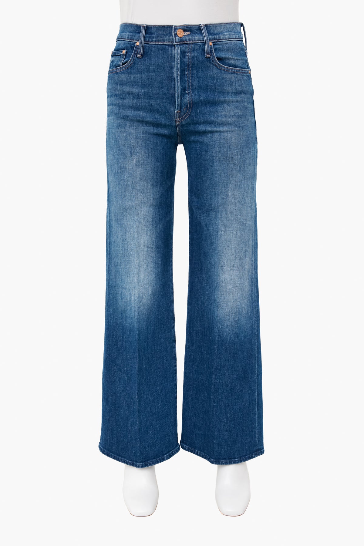 A pair of high-rise, wide-leg blue jeans with a faded wash by MOTHER, shown on a mannequin wearing white shoes.