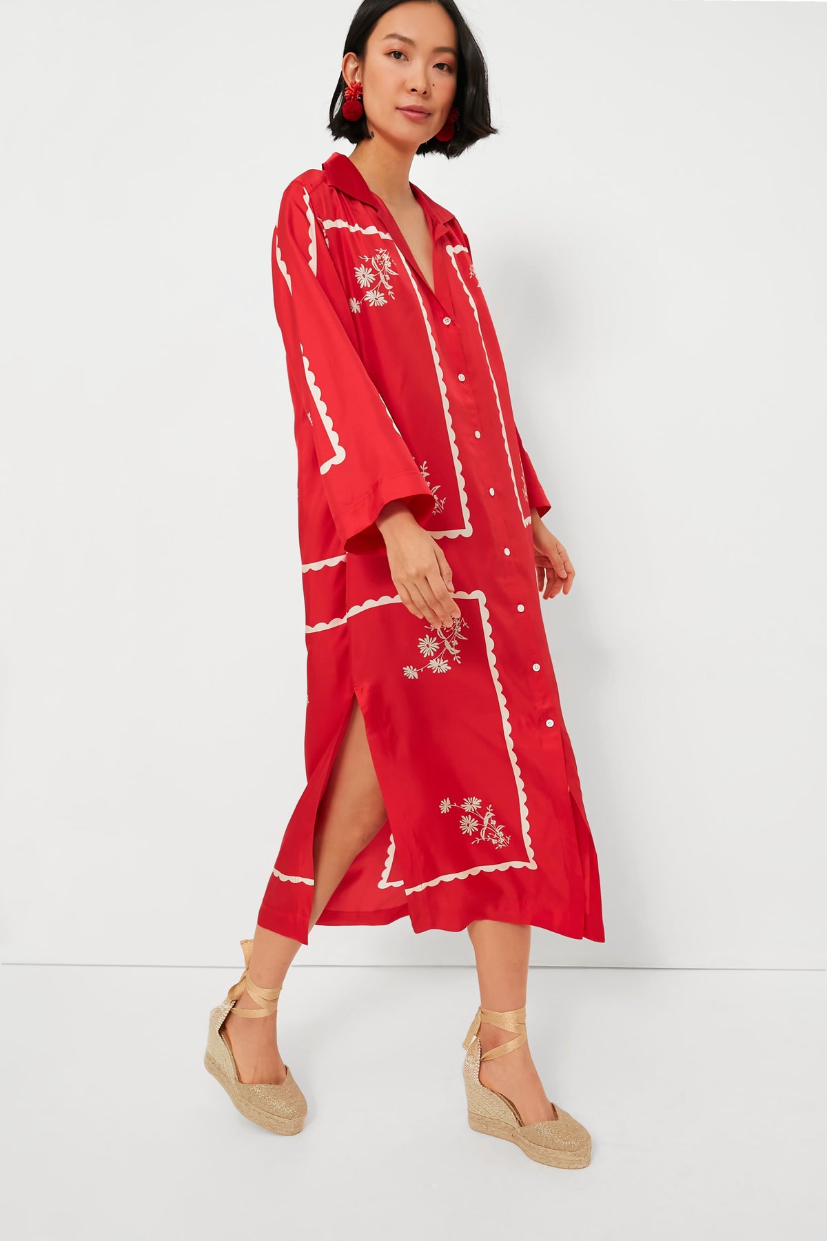 Woman wearing an Oroton long red button-down dress with white embroidery, beige wedge sandals, and red earrings. The vintage daisy print adds a charming touch to her elegant look.