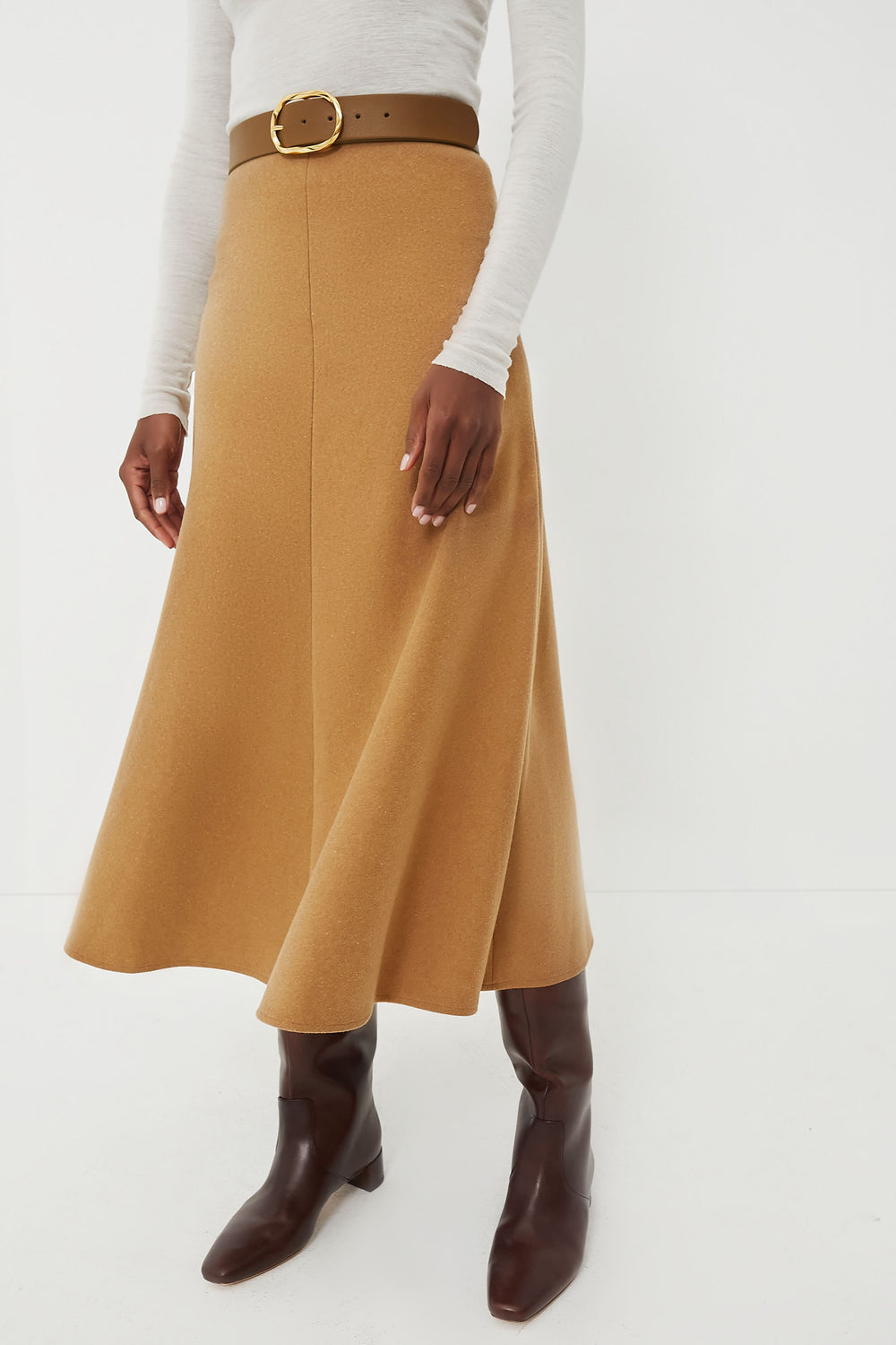 Wearing a Vanessa Bruno light long-sleeve top, high-waisted A-line midi skirt with a wide brown belt, and brown knee-high boots creates a chic and elegant look.