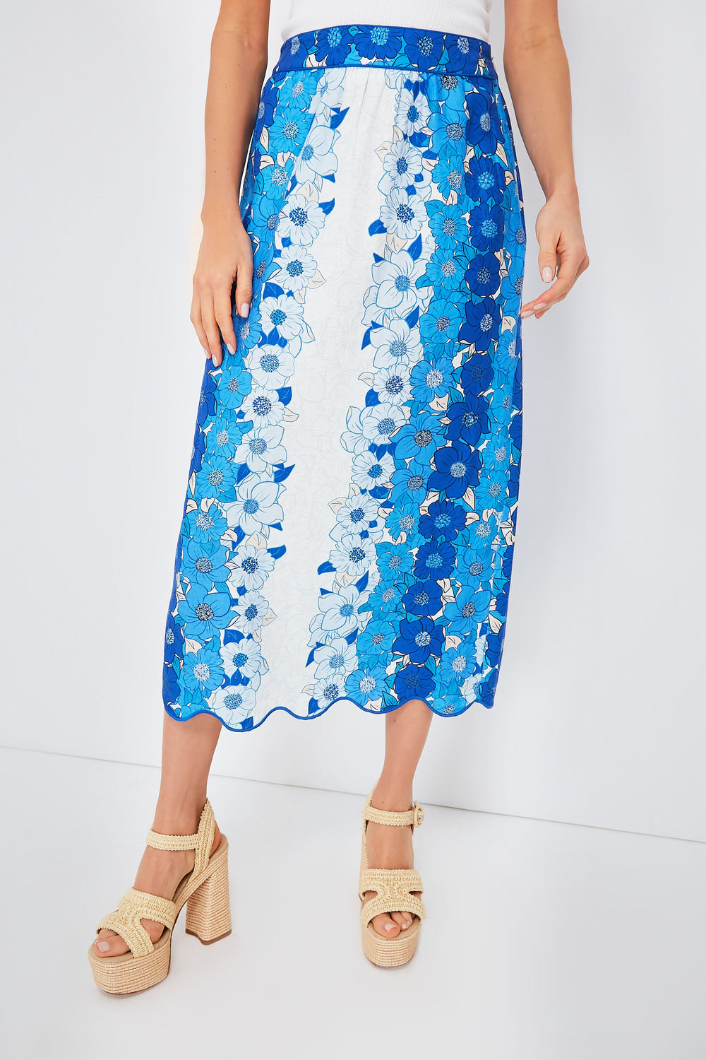 A person stands confidently in a blue and white Farm Rio floral midi skirt with a scalloped hem, paired with beige platform sandals.