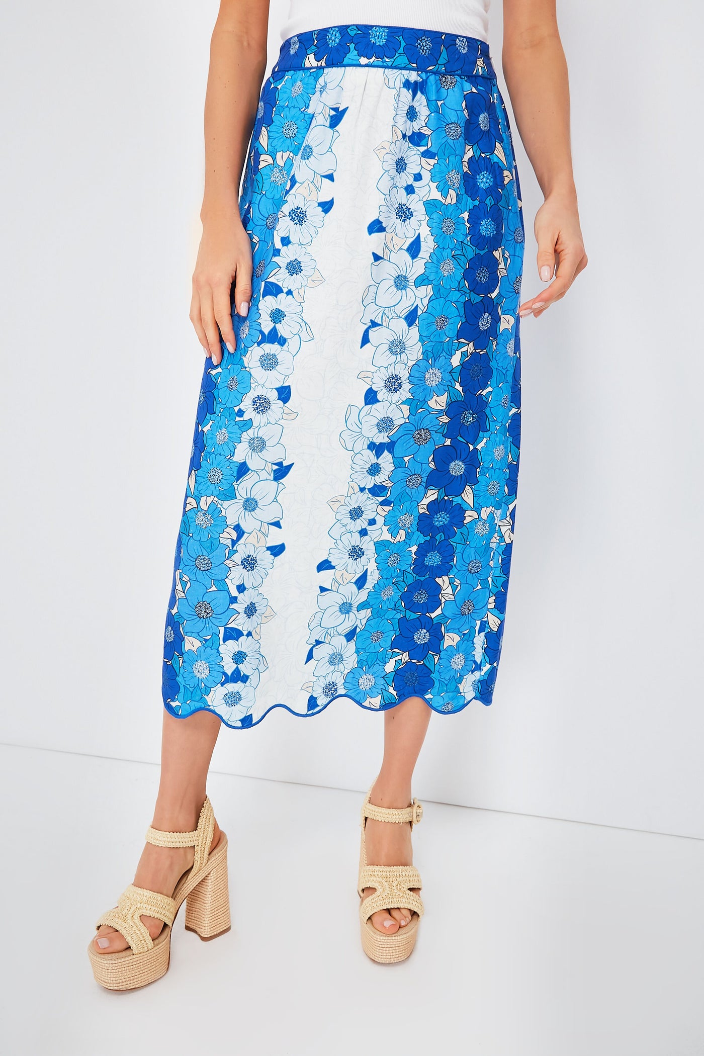 A person stands confidently in a blue and white Farm Rio floral midi skirt with a scalloped hem, paired with beige platform sandals.
