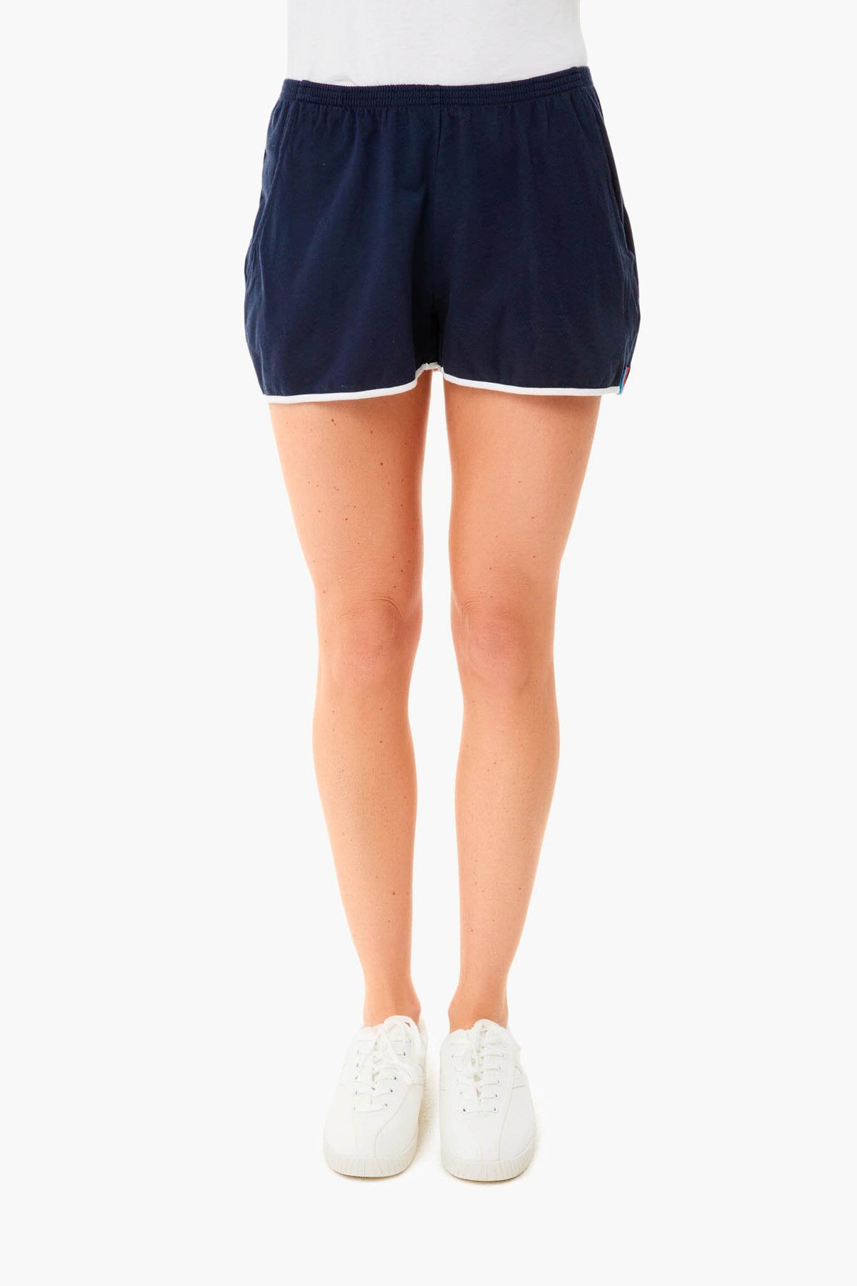A person wearing KULE navy blue athletic shorts with white trim, a striped tee, and white sneakers.