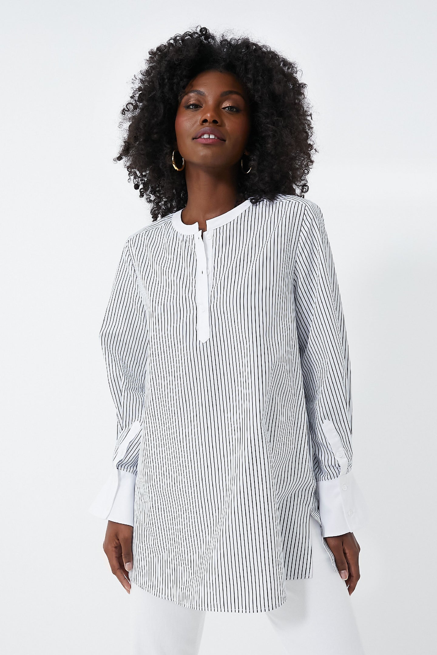 A woman wears a HARSHMAN long-sleeve black-and-white vertically striped Zoe Popover blouse with a collarless neckline and white cuffs, showcasing classic womenswear style.