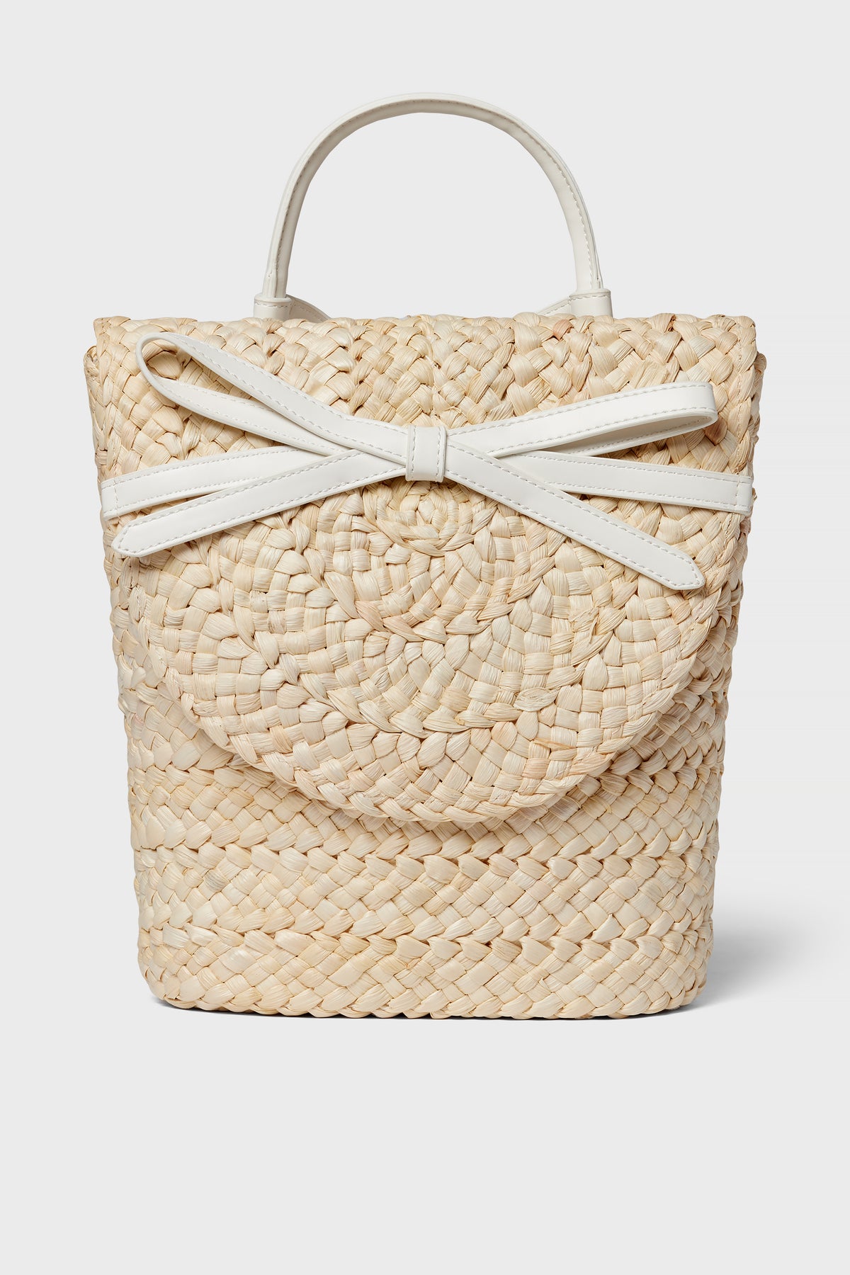 The BTB woven straw handbag boasts a boho-chic style with a round flap, white handles, and a decorative white bow detail on the front.