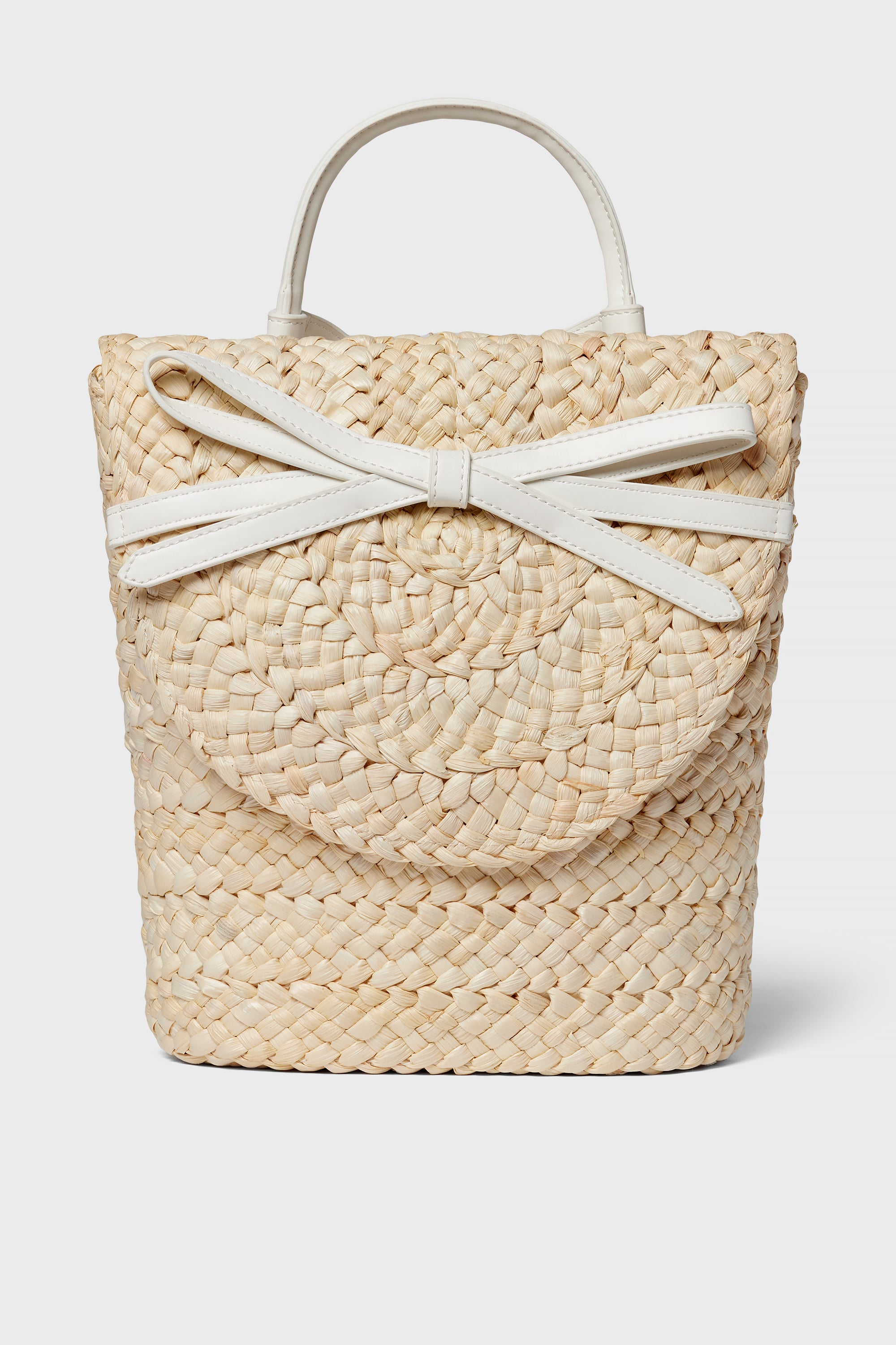 The BTB woven straw handbag boasts a boho-chic style with a round flap, white handles, and a decorative white bow detail on the front.
