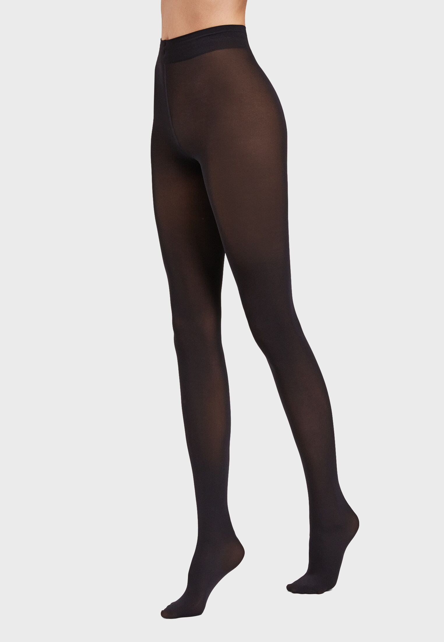 A person showcases only their lower body, wearing semi-opaque black tights by Wolford.