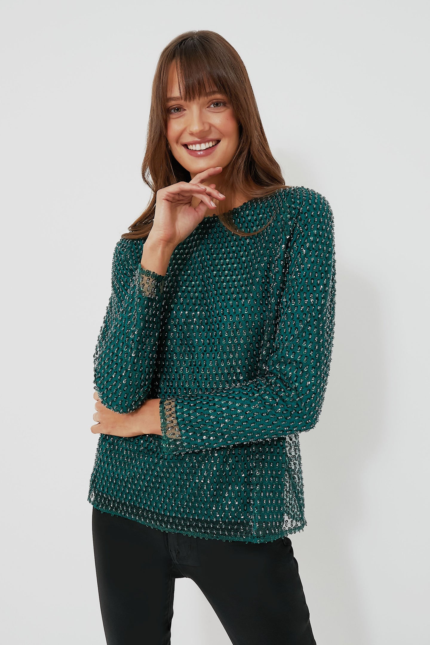 A woman smiles with her hand near her face, wearing a Hyacinth House dark green textured party top and black pants.