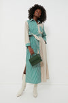 A woman wears a Tuckernuck striped maxi shirt dress with green and beige vertical stripes, white boots, and a small green handbag while standing against a plain white background.