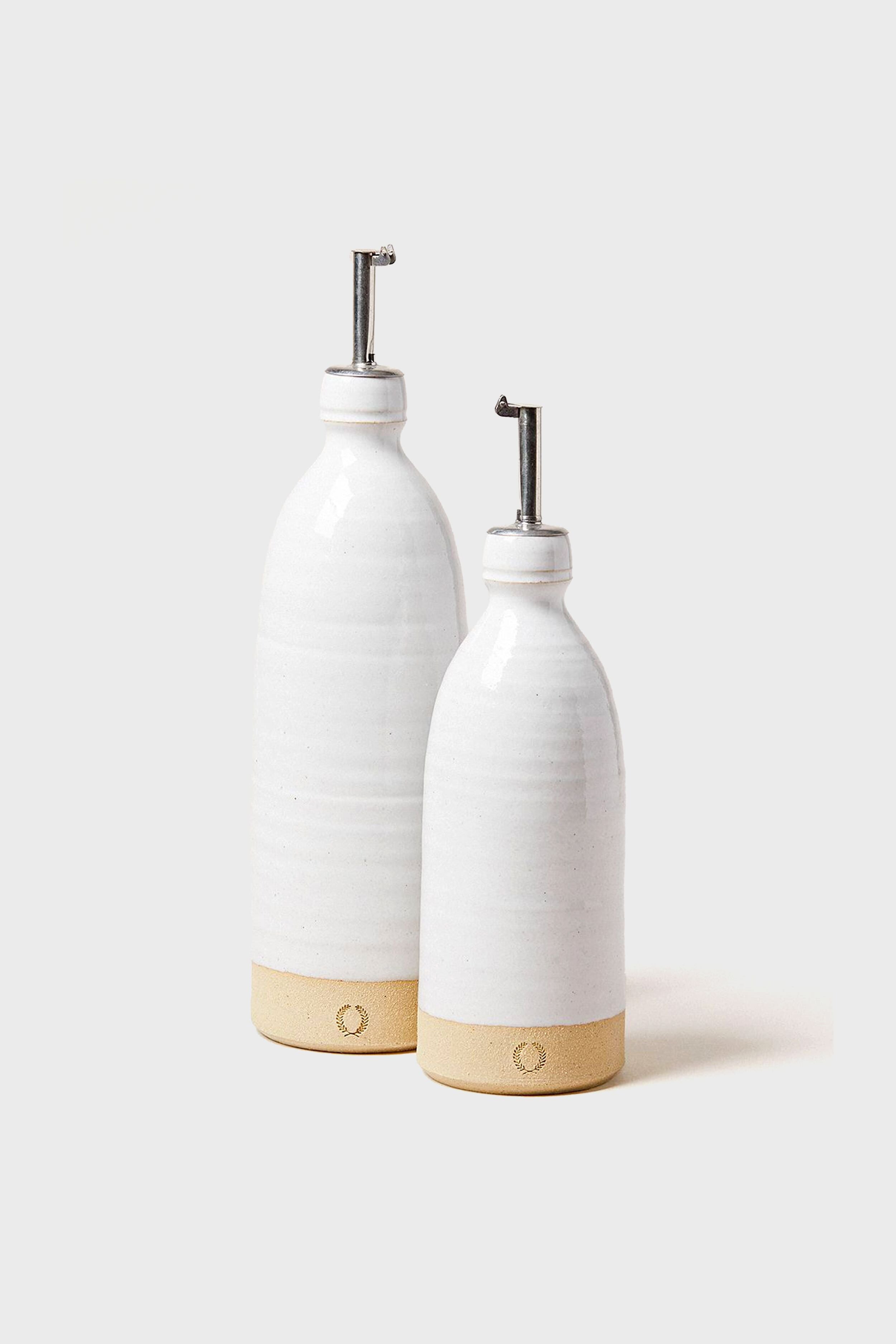 Two Farmhouse Pottery, Inc. ceramic oil dispensers feature white tops, natural clay bases, and metal spouts. Ideal as olive oil bottles, they reflect classic farmhouse style inspired by American stoneware pottery.