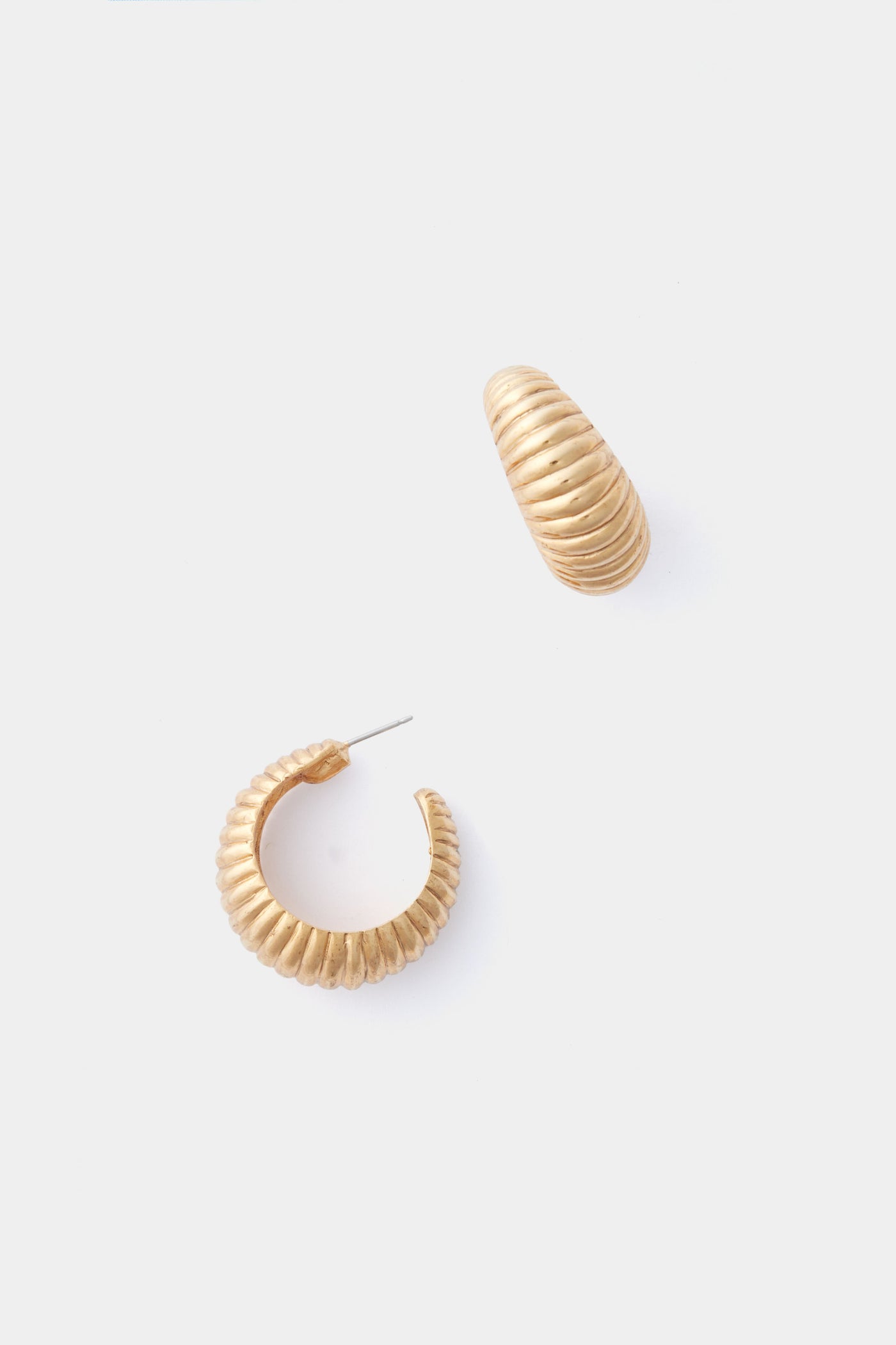 A pair of gold-tone, ribbed hoop earrings by Jennifer Behr is displayed—one earring lies down while the other stands upright. These stylish accessories are ideal for elevating any outfit.