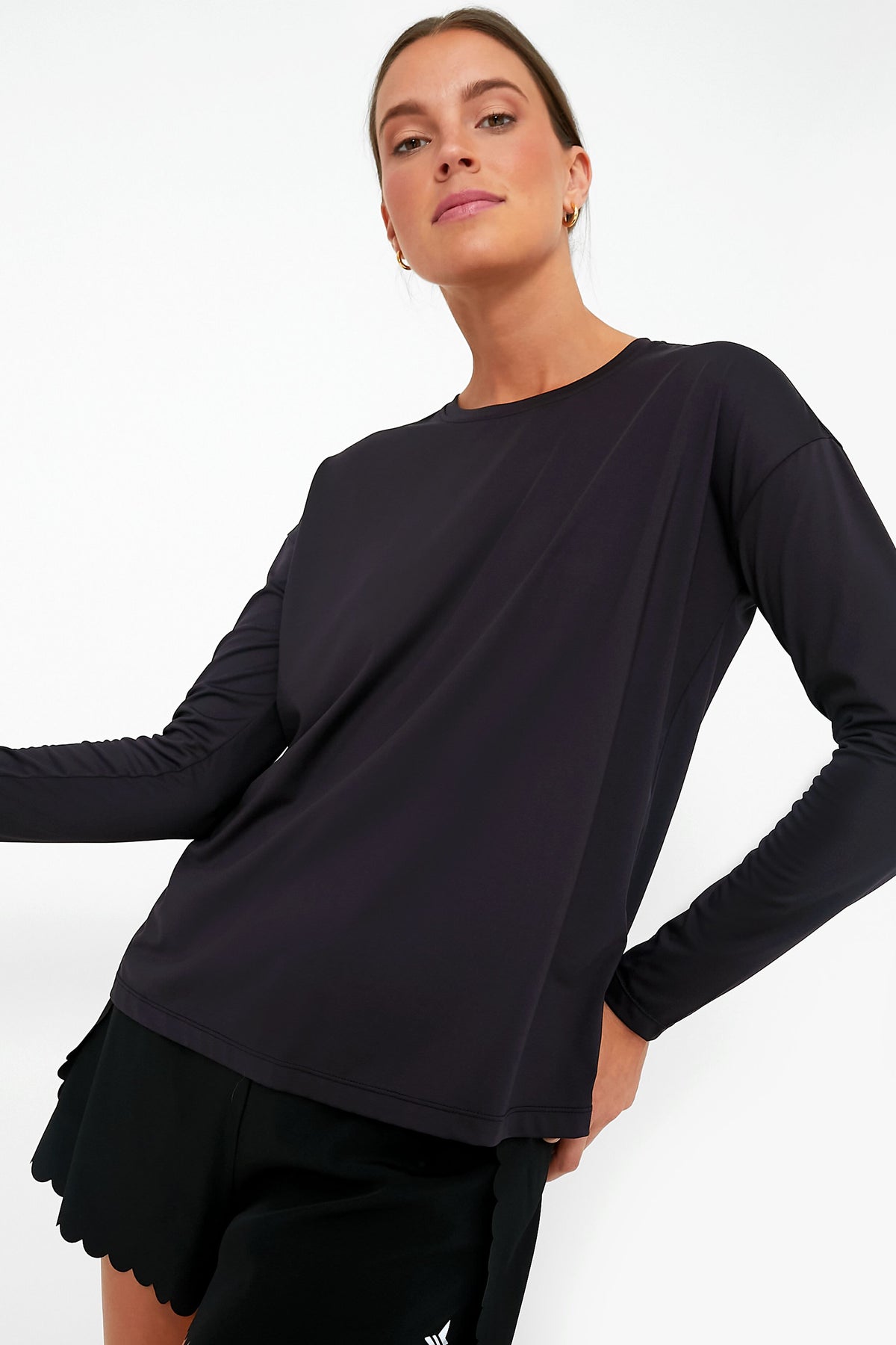 A person confidently poses in Tnuck Sport’s moisture-wicking long sleeve tee and black shorts, highlighting stylish comfort and SPF protection.