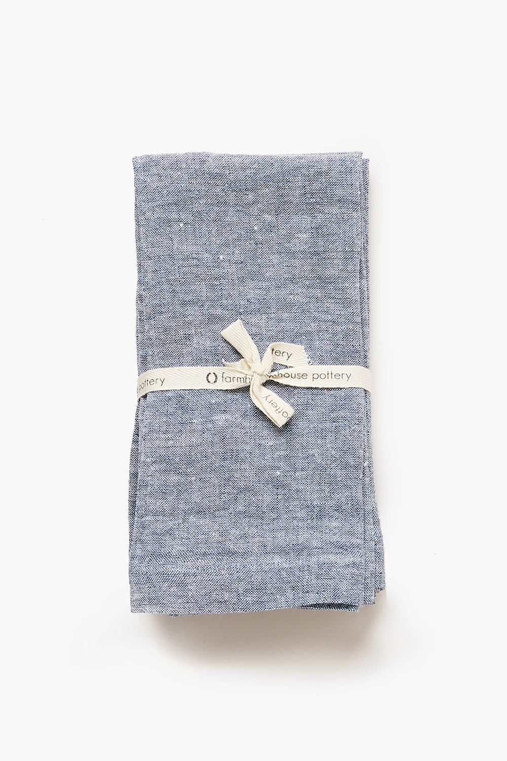 A folded blue Indigo Washed Linen Napkin by Farmhouse Pottery, Inc, tied with a cream ribbon—ideal for stylish farmhouse table settings.