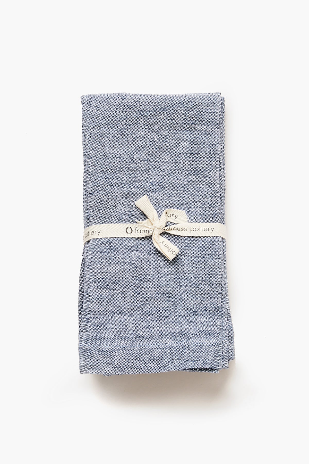 A folded blue Indigo Washed Linen Napkin by Farmhouse Pottery, Inc, tied with a cream ribbon—ideal for stylish farmhouse table settings.