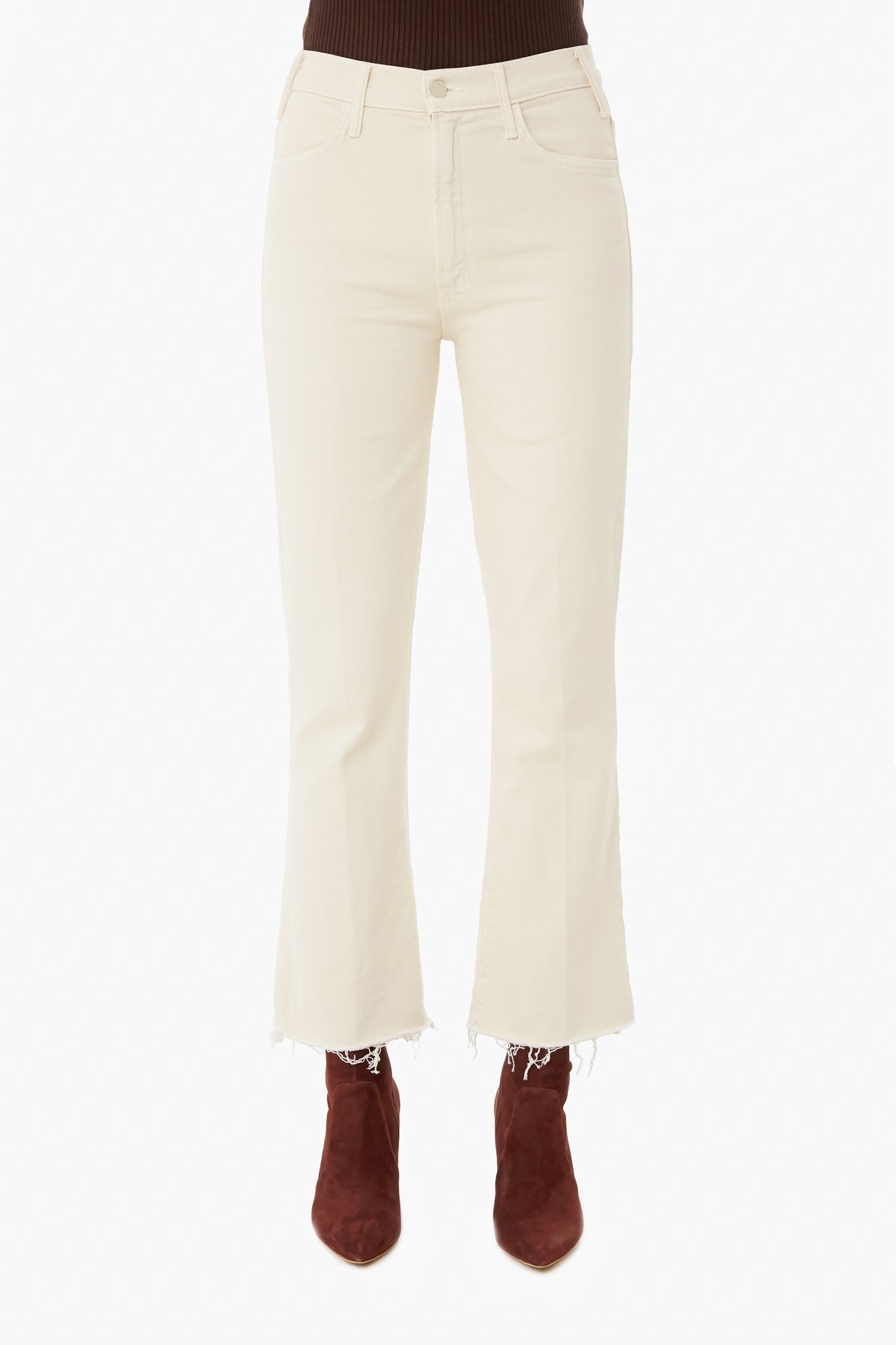 A person wearing MOTHER high-waisted, off-white cropped ankle jeans with raw hems and brown suede boots; upper body is partially visible.