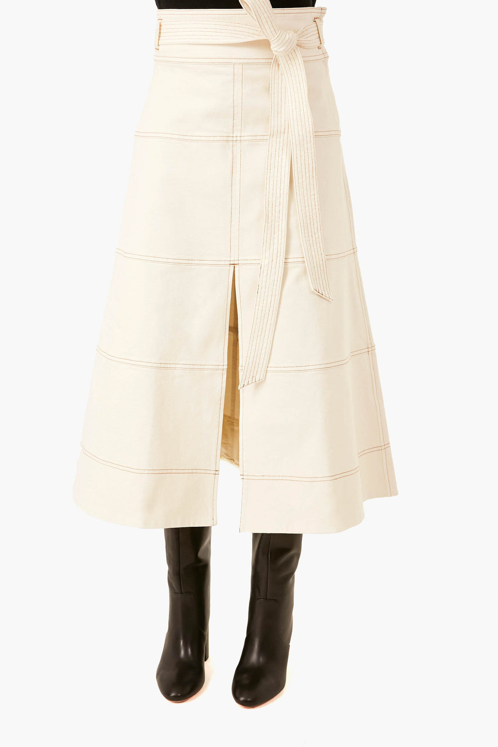 Someone dressed in a Tanya Taylor organic cotton cream belted midi skirt with a front slit, paired with black knee-high boots.