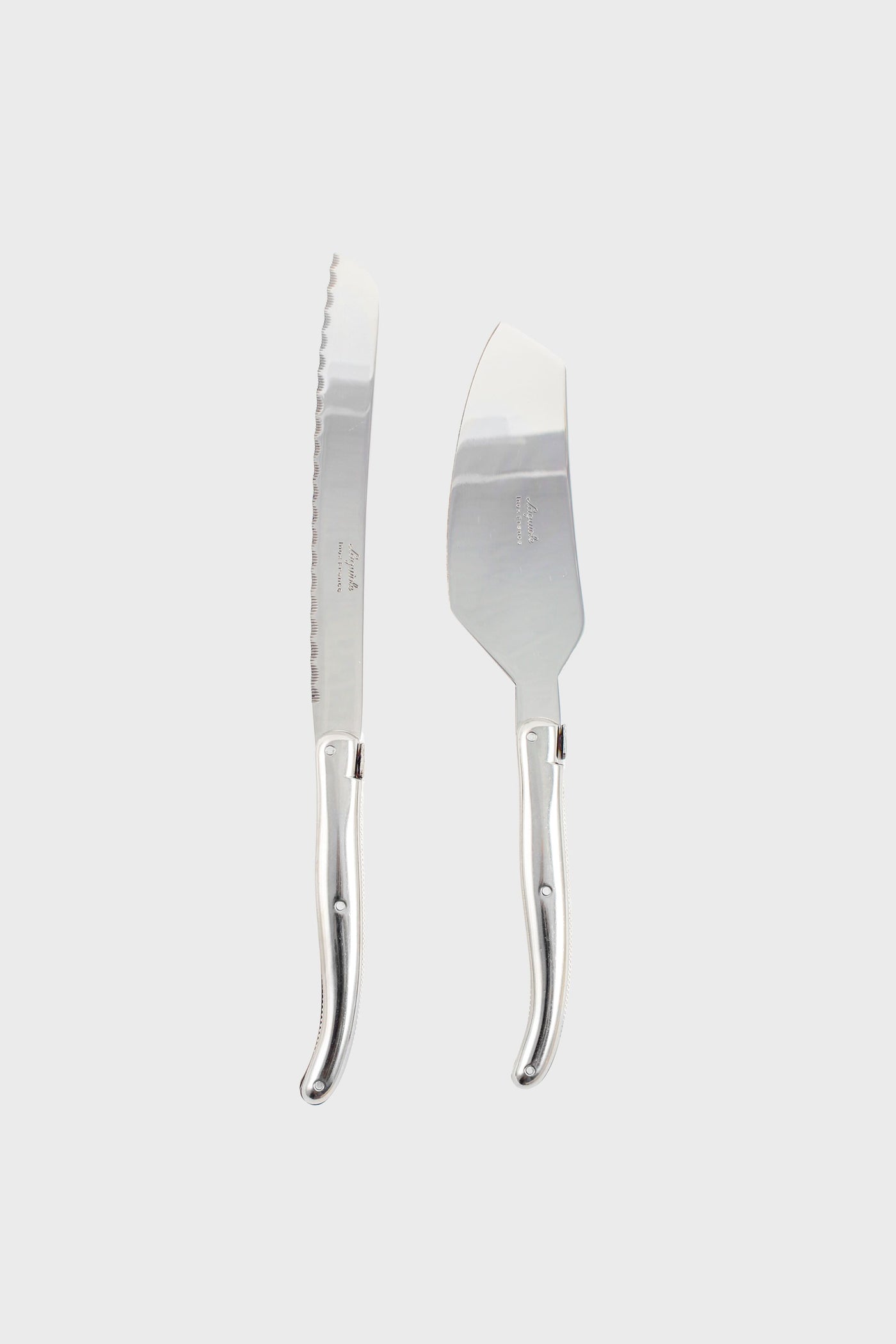 A Laguiole silver bread knife and cheese knife with matching curved handles are placed side by side, highlighting the brand's French craftsmanship and elegant design.