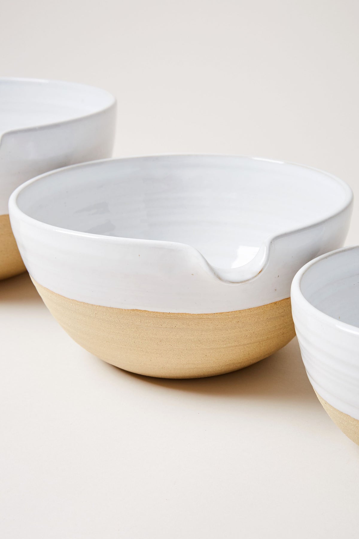 Set of three ceramic pantry bowls by Farmhouse Pottery, Inc. Each features an unglazed tan base and glossy white interior; the central bowl includes a handy spout—ideal for lovers of farmhouse-style pottery.