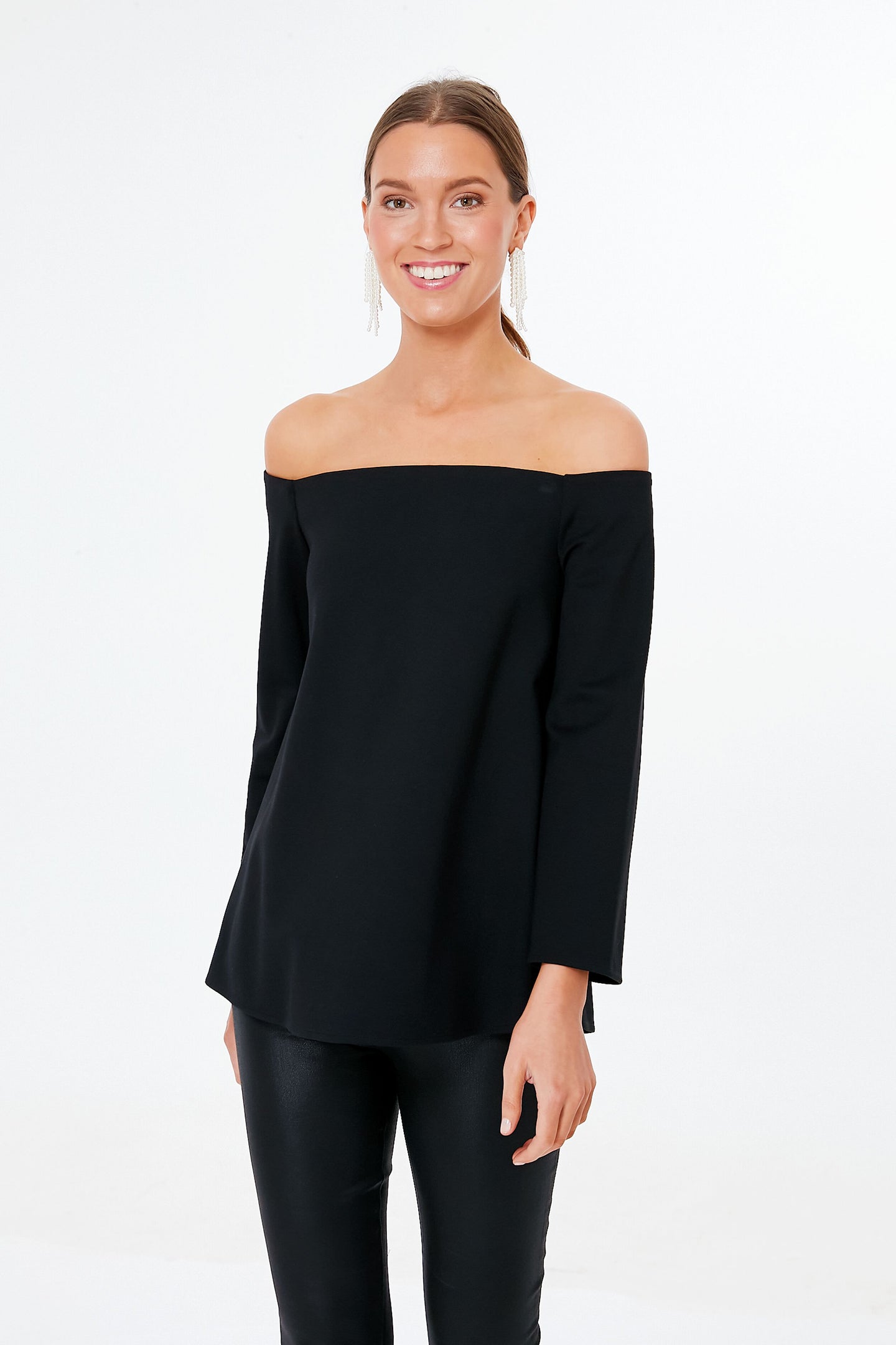 A woman smiles at the camera in a Tuckernuck black off-the-shoulder blouse and black pants—an elegant, minimalist date night look.