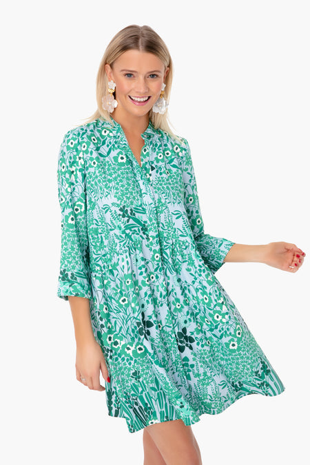 A woman smiles brightly in a Tuckernuck green and white wildflower print shirt dress—an ideal addition to your spring wardrobe.
