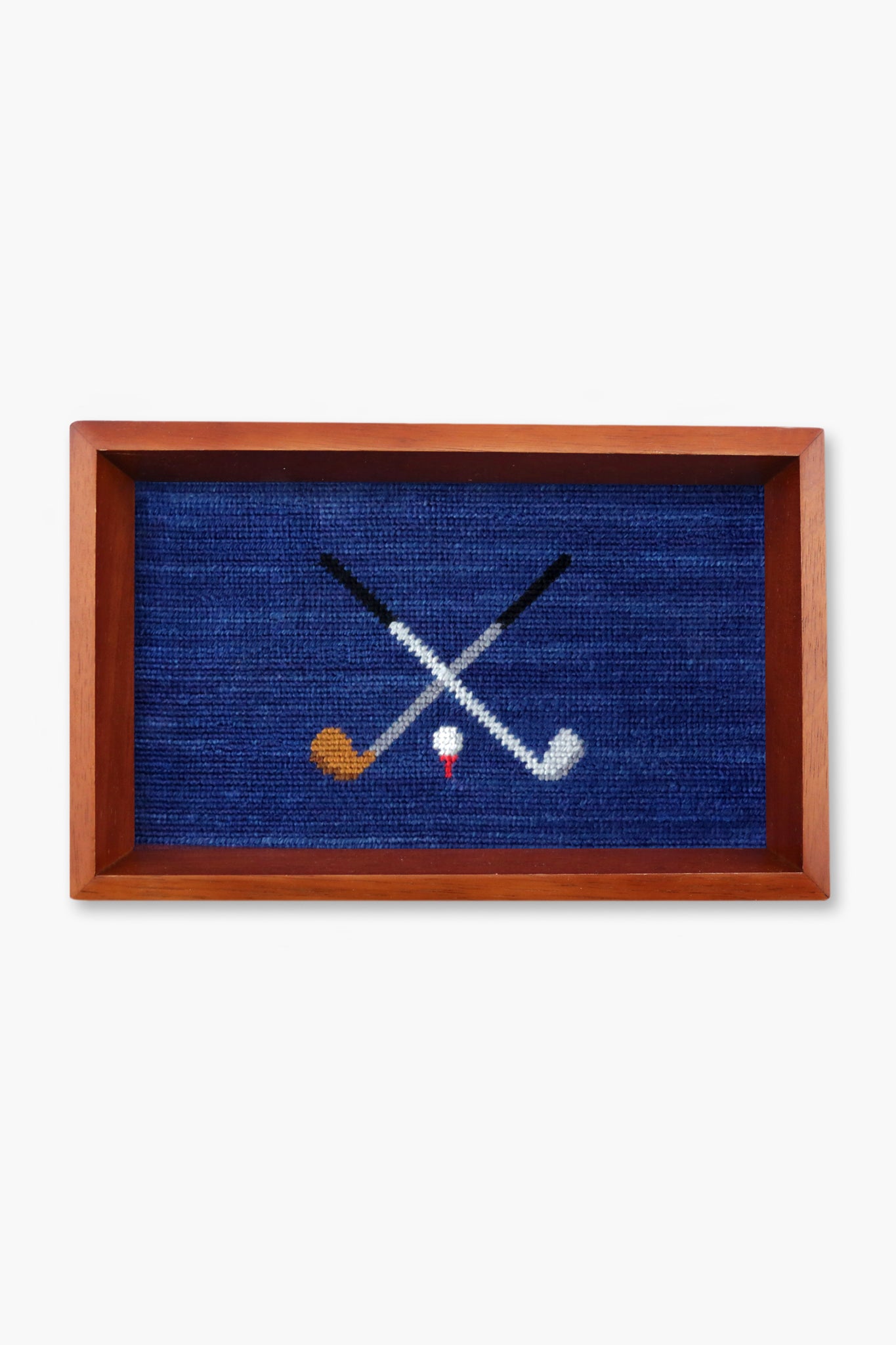 Smathers and Branson’s rectangular valet tray features a wooden frame and a needlepoint design of two crossed golf clubs above a white golf tee with a red stripe.