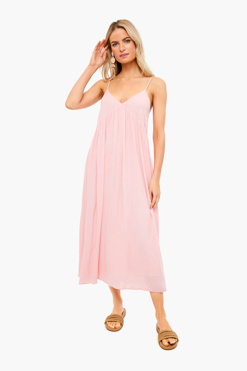 A woman showcases the elegant Atlas Midi Dress by Z SUPPLY, featuring a light pink crinkle viscose fabric with adjustable straps, paired with tan sandals.