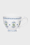 This Juliska white ceramic breakfast cup features a handle, blue and green floral patterns, and a blue rim border. Both practical and beautifully designed, it is dishwasher safe.