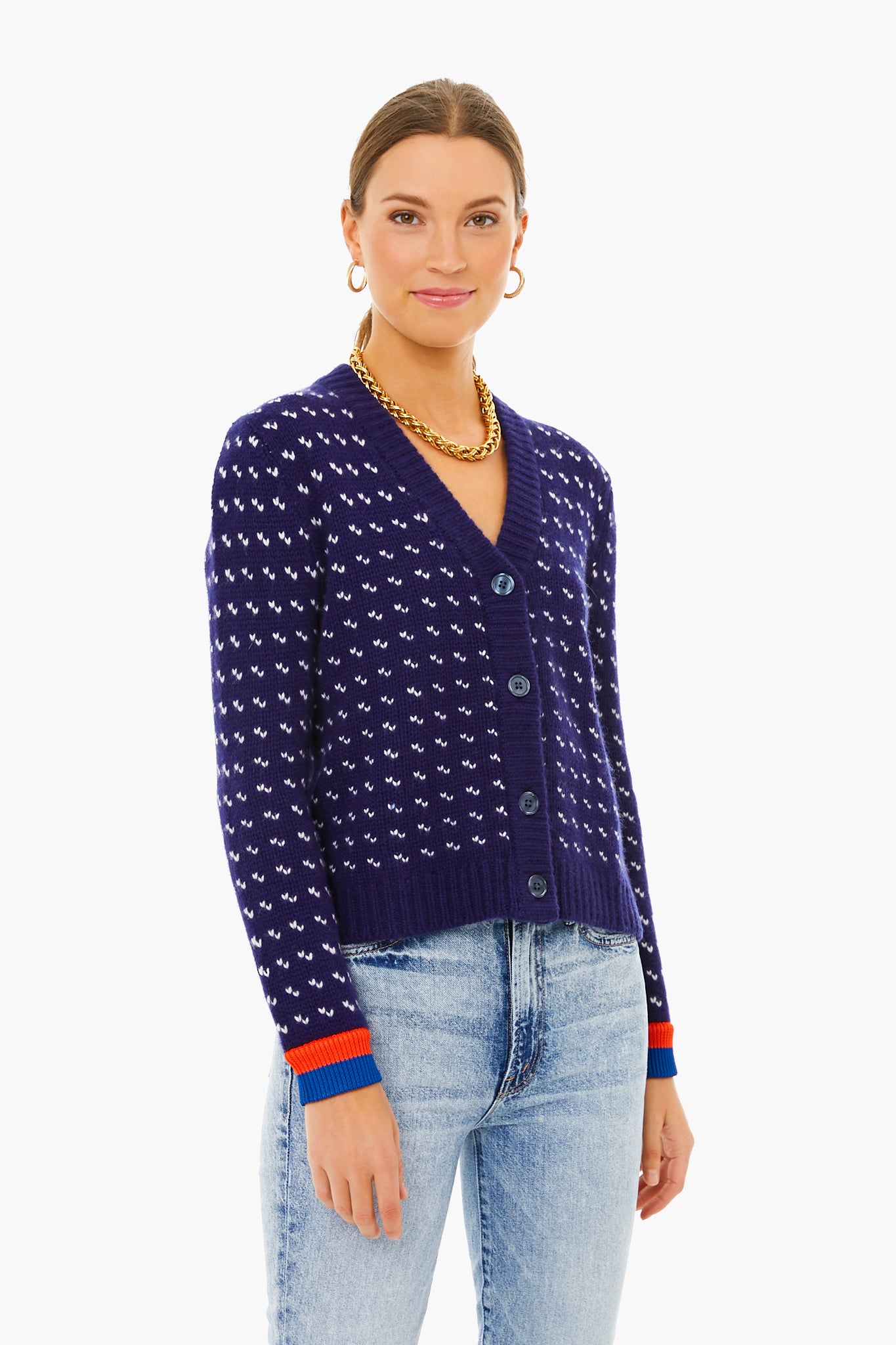 A person wears a KULE navy blue Billy Cardigan with a white dot pattern and red and blue cuffs, paired with light-wash jeans.