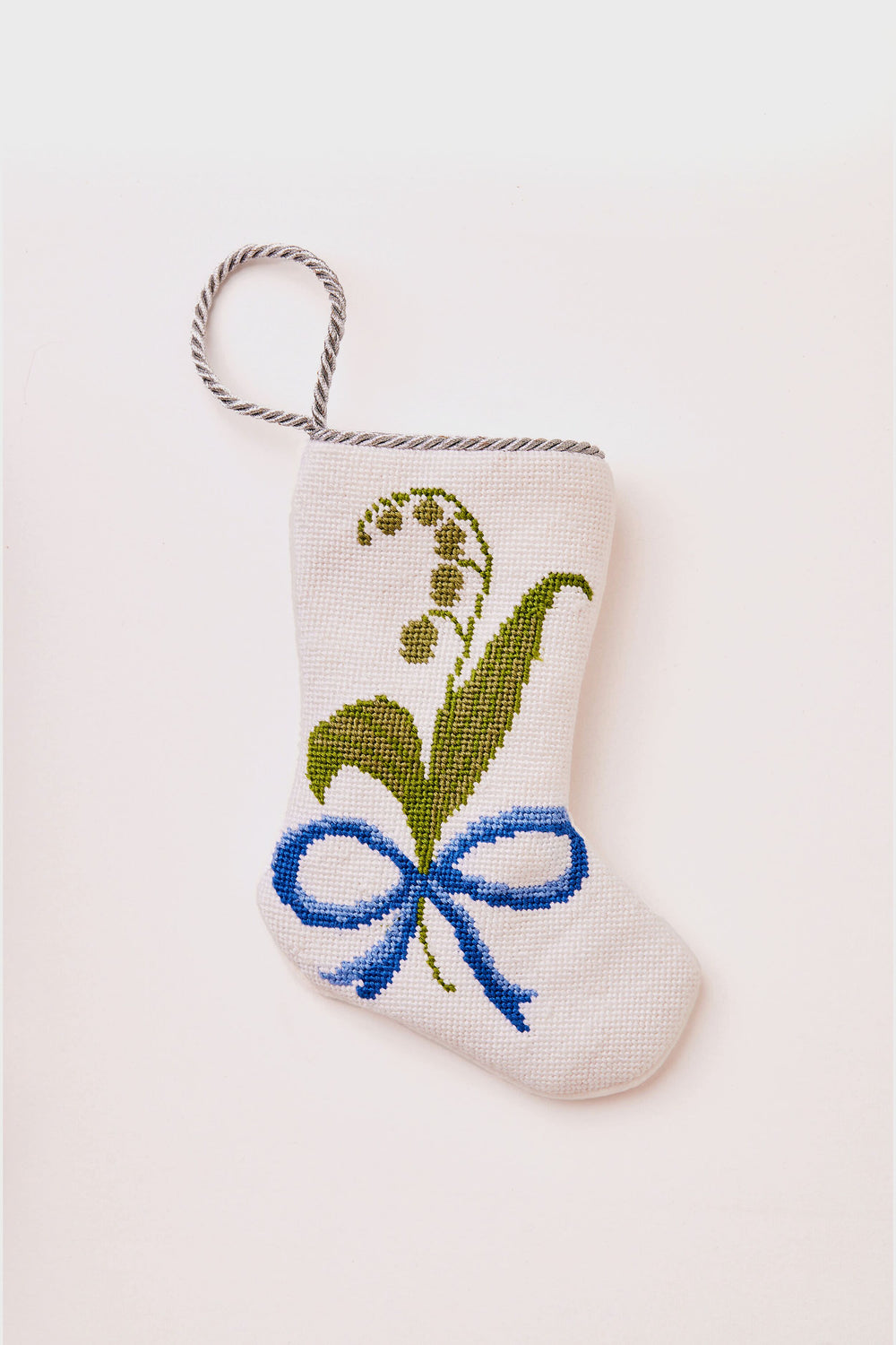 A small white Bauble Stockings hand-stitched Christmas stocking features a green floral cross-stitch design, a blue bow, and a twisted hanging loop—perfect for bringing unique holiday tradition to your celebrations.