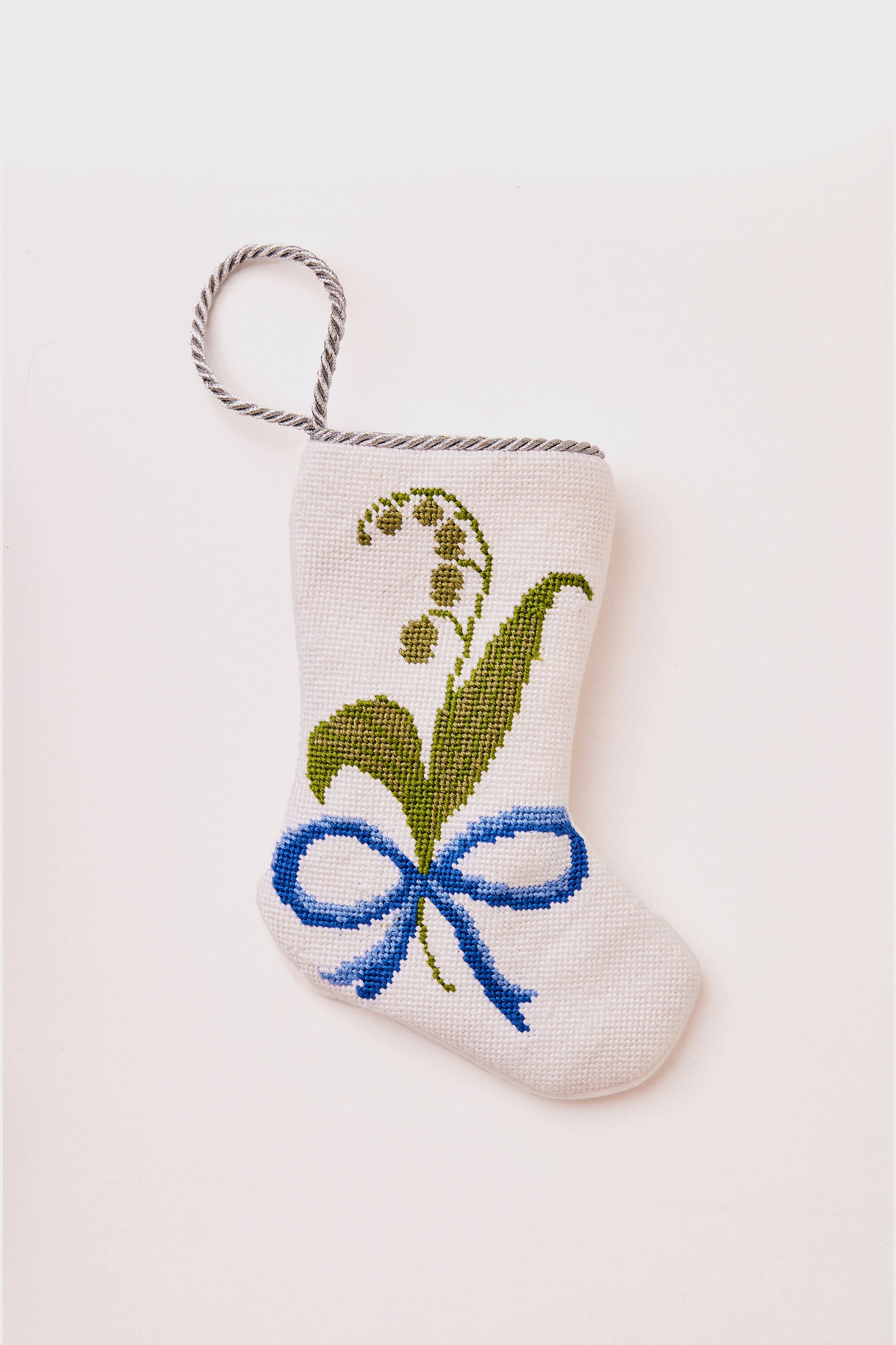 A small white Bauble Stockings hand-stitched Christmas stocking features a green floral cross-stitch design, a blue bow, and a twisted hanging loop—perfect for bringing unique holiday tradition to your celebrations.
