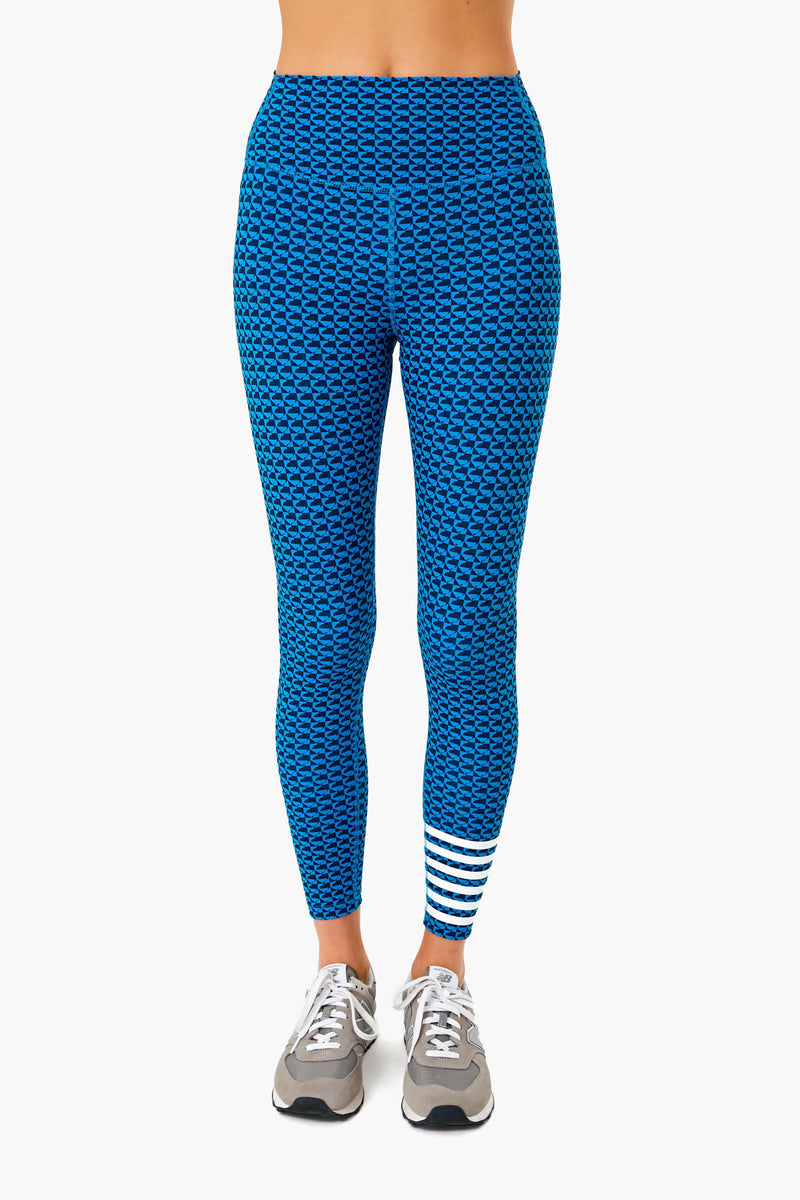 A person is shown from waist to feet wearing Addison Bay high-rise, blue patterned leggings with white stripes near the left ankle and gray sneakers. The leggings feature sweat-wicking fabric for comfortable activewear.