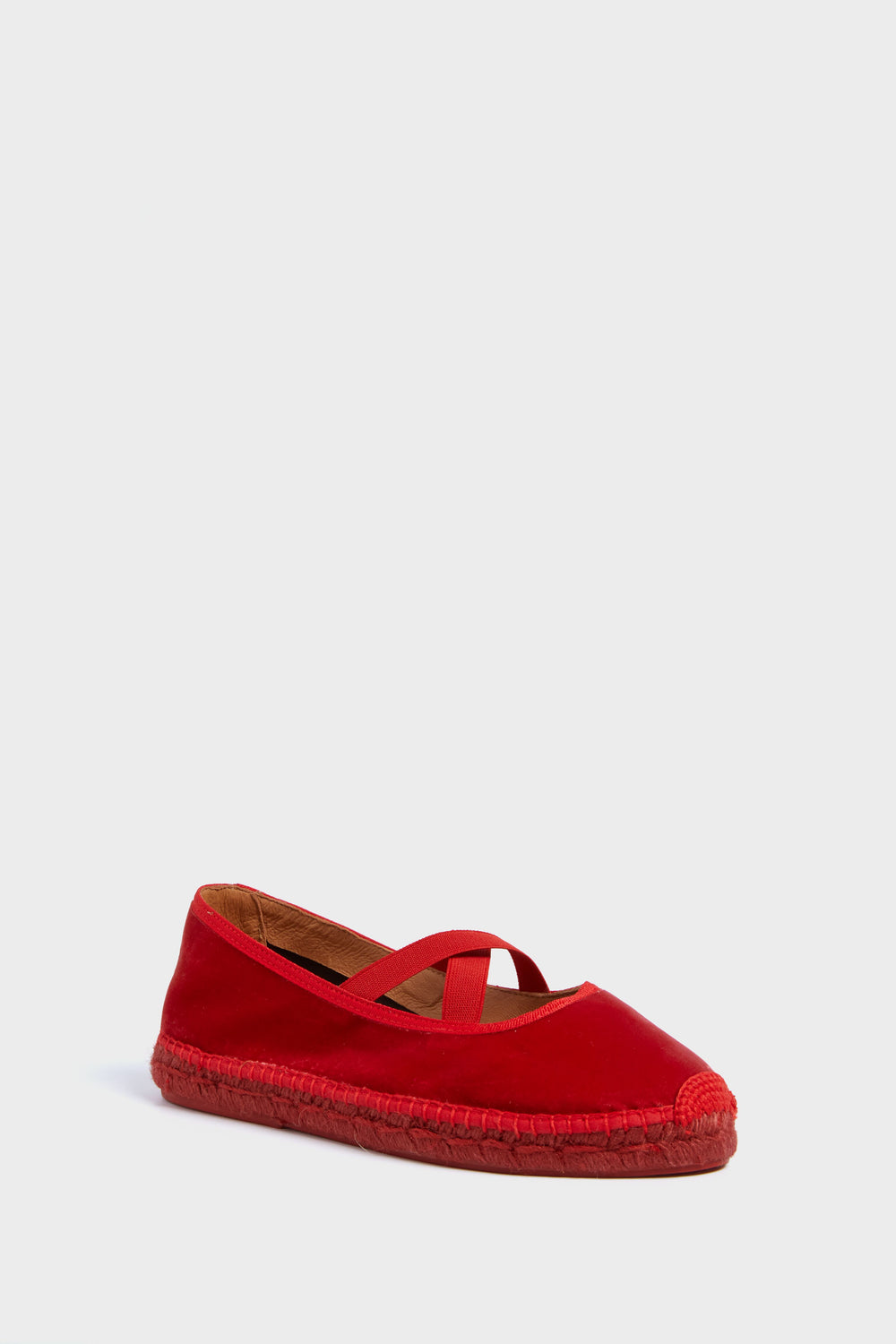 A single red espadrille flat shoe by Penelope Chilvers, featuring a jute sole and crisscross elastic straps, inspired by classic ballet flat designs.