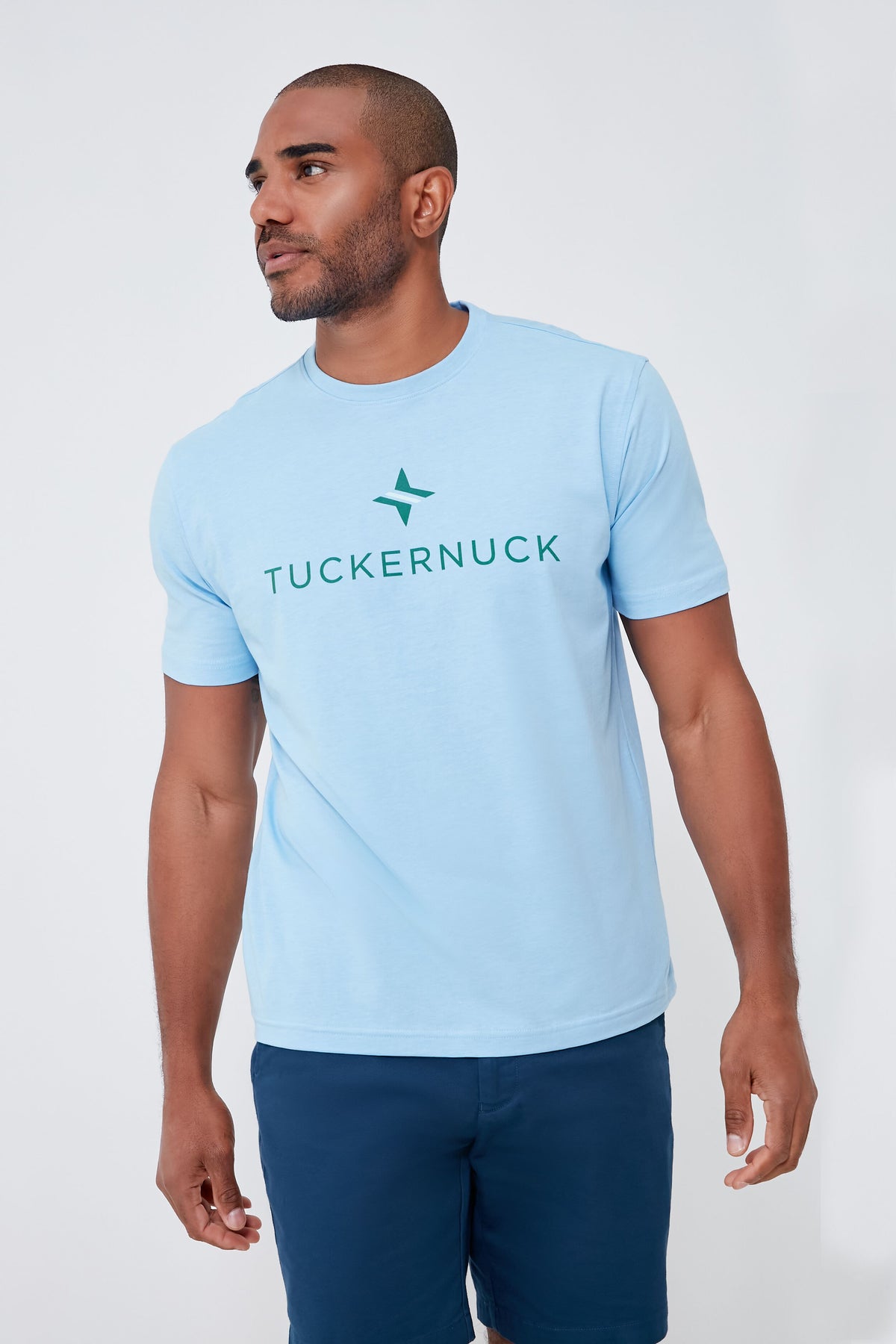 A man wearing a light blue Peter Millar performance tee with UPF 50+ sun protection and navy shorts stands confidently.