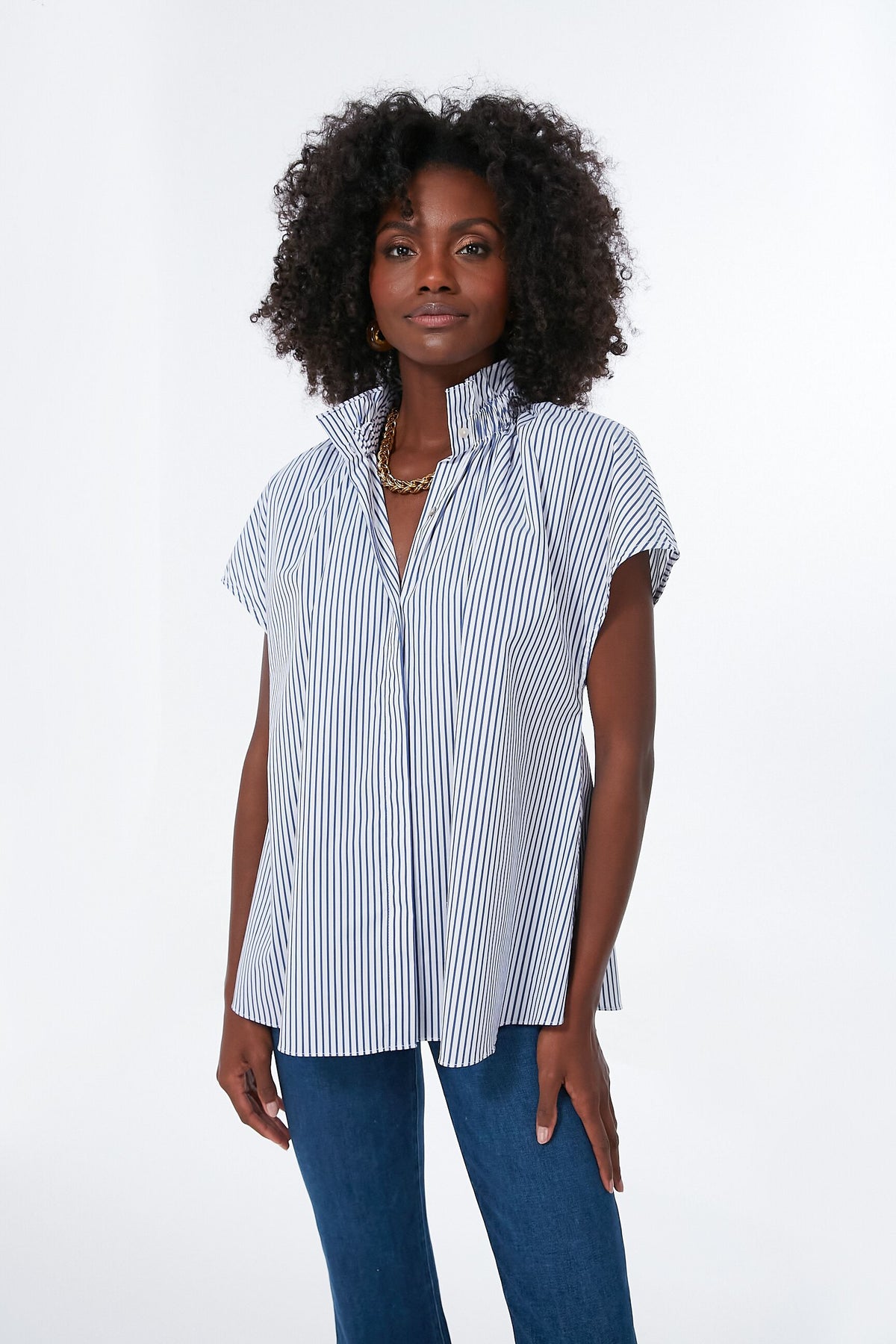 A woman wears the Pomander Place Rae Blouse, featuring blue and white vertical stripes with a ruffle collar, paired with blue jeans.