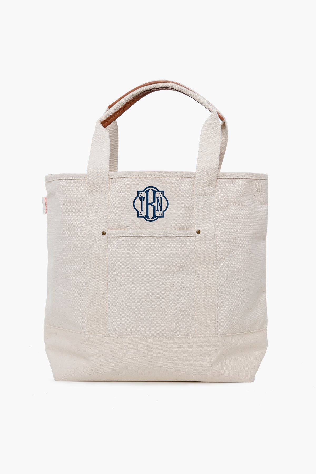 This CB Station cream canvas tote features short handles and a navy blue monogram on the front pocket, making it a stylish and eco-friendly reusable bag.