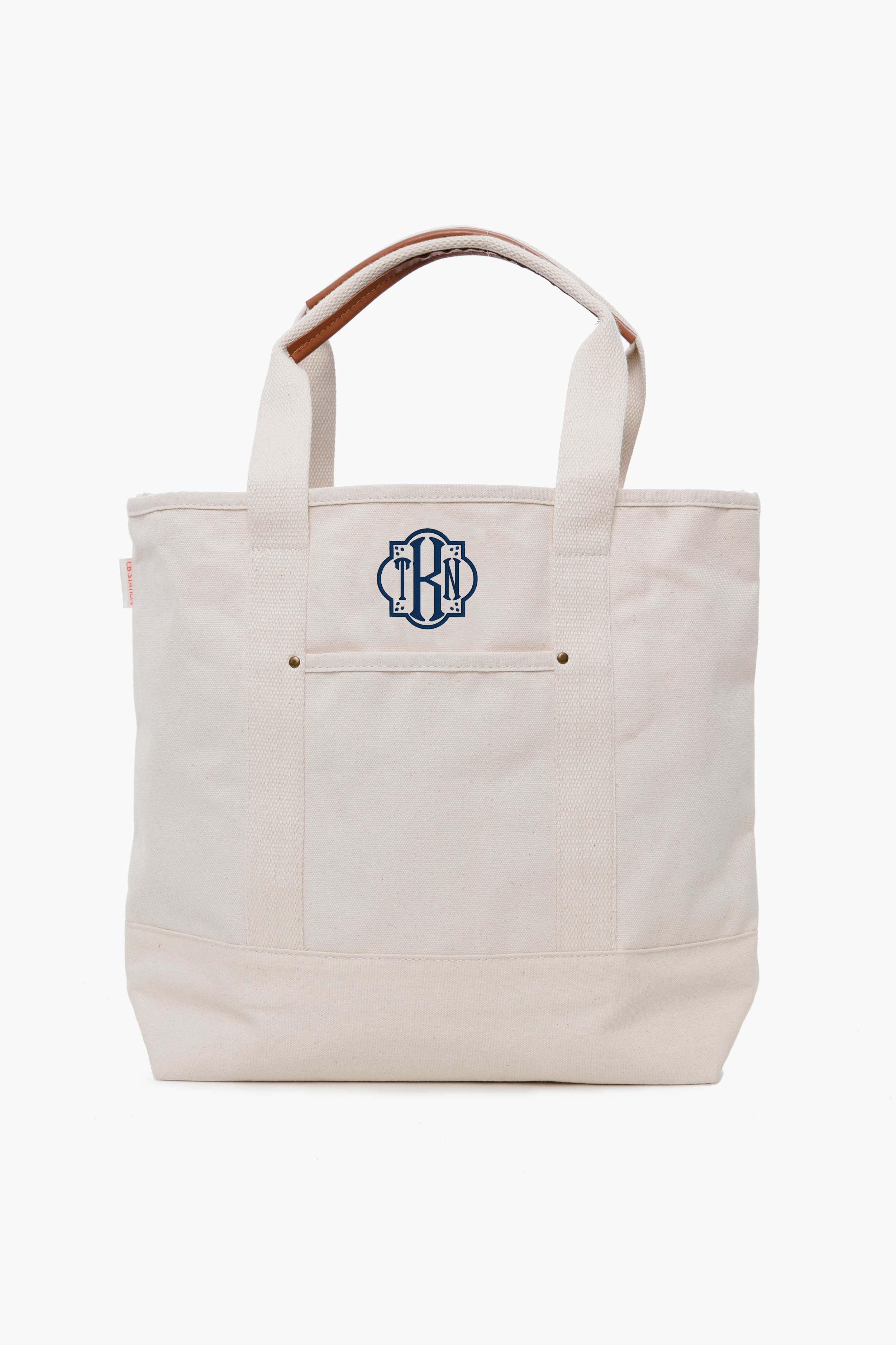 This CB Station cream canvas tote features short handles and a navy blue monogram on the front pocket, making it a stylish and eco-friendly reusable bag.