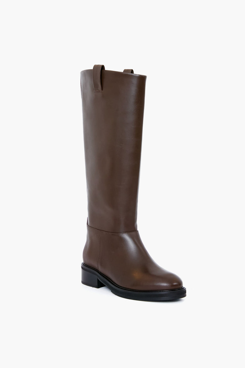 Flattered's handmade chocolate leather knee-high boot features a low heel and pull tabs, blending elegance and craftsmanship.