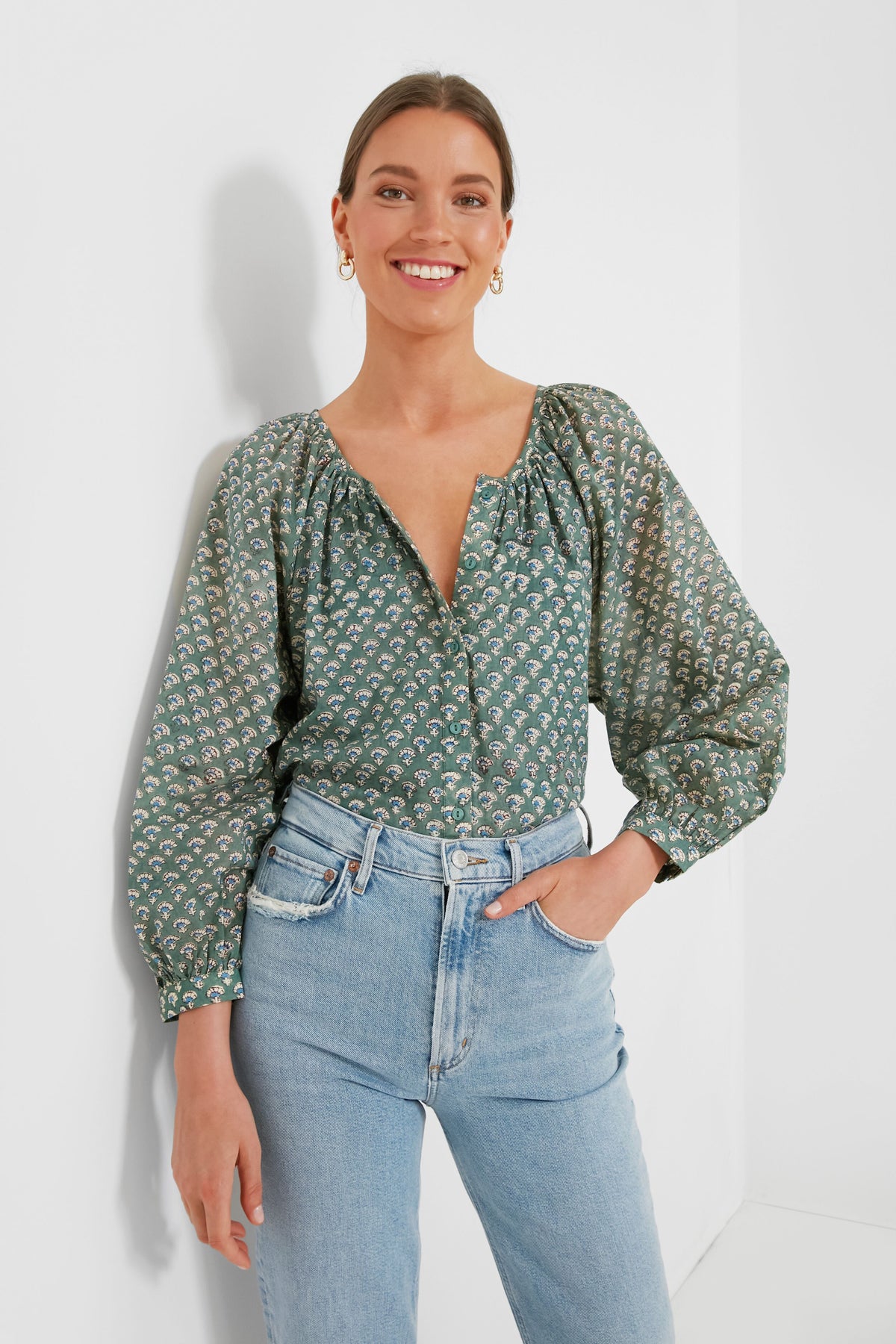 A woman smiles in a green hand-block printed blouse with balloon sleeves from Love Tomas by Emerson Fry, paired with light blue high-waisted jeans.