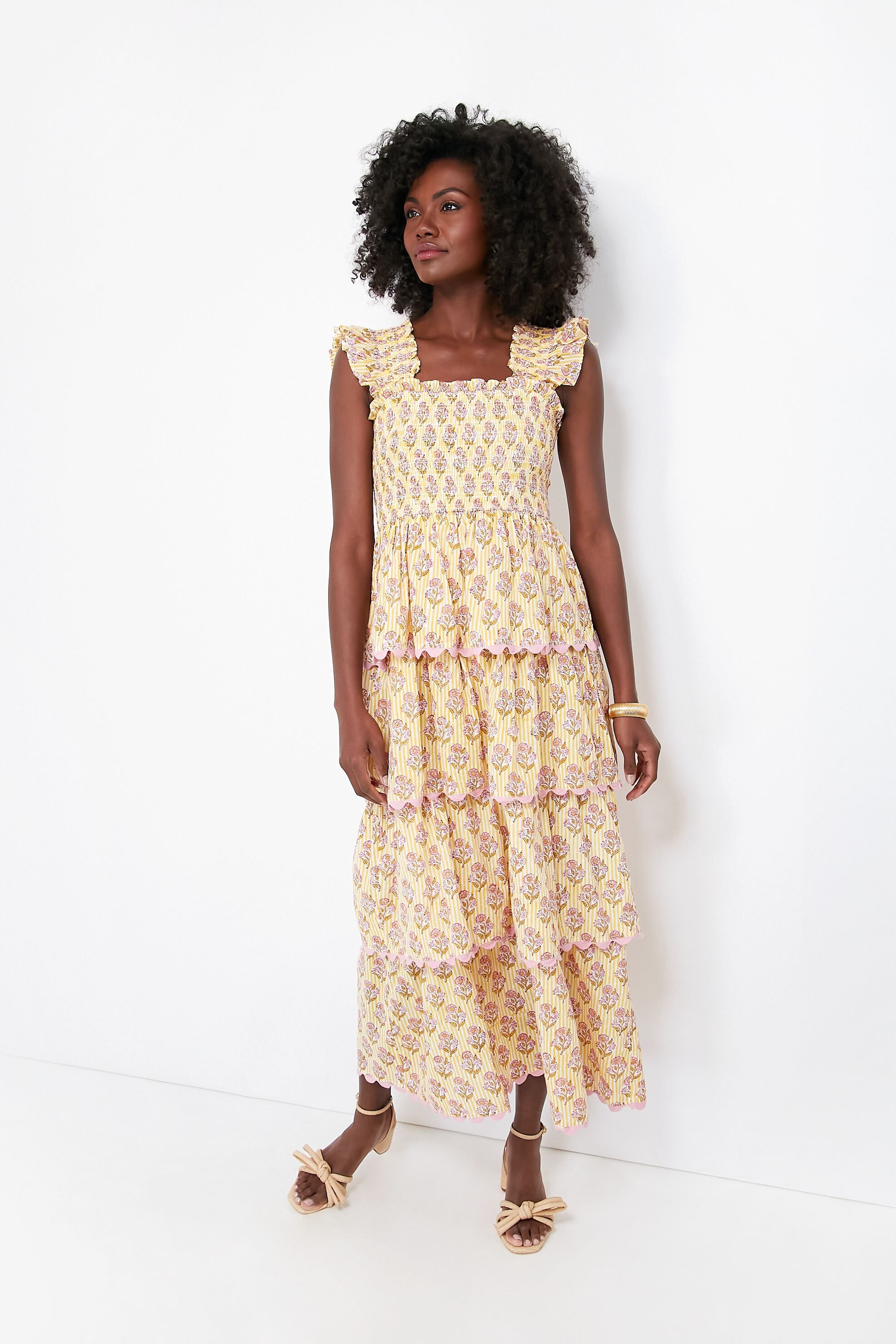 A woman wears the Saylor Lemonade Teodora Dress, a feminine maxi with yellow and pink floral tiers, paired with matching bow sandals.