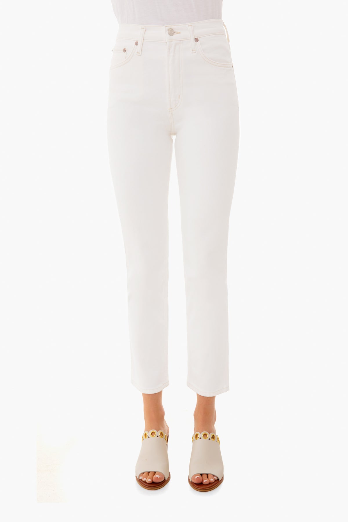 A person stands confidently in white AGOLDE mid-rise straight jeans and white sandals with gold accents.