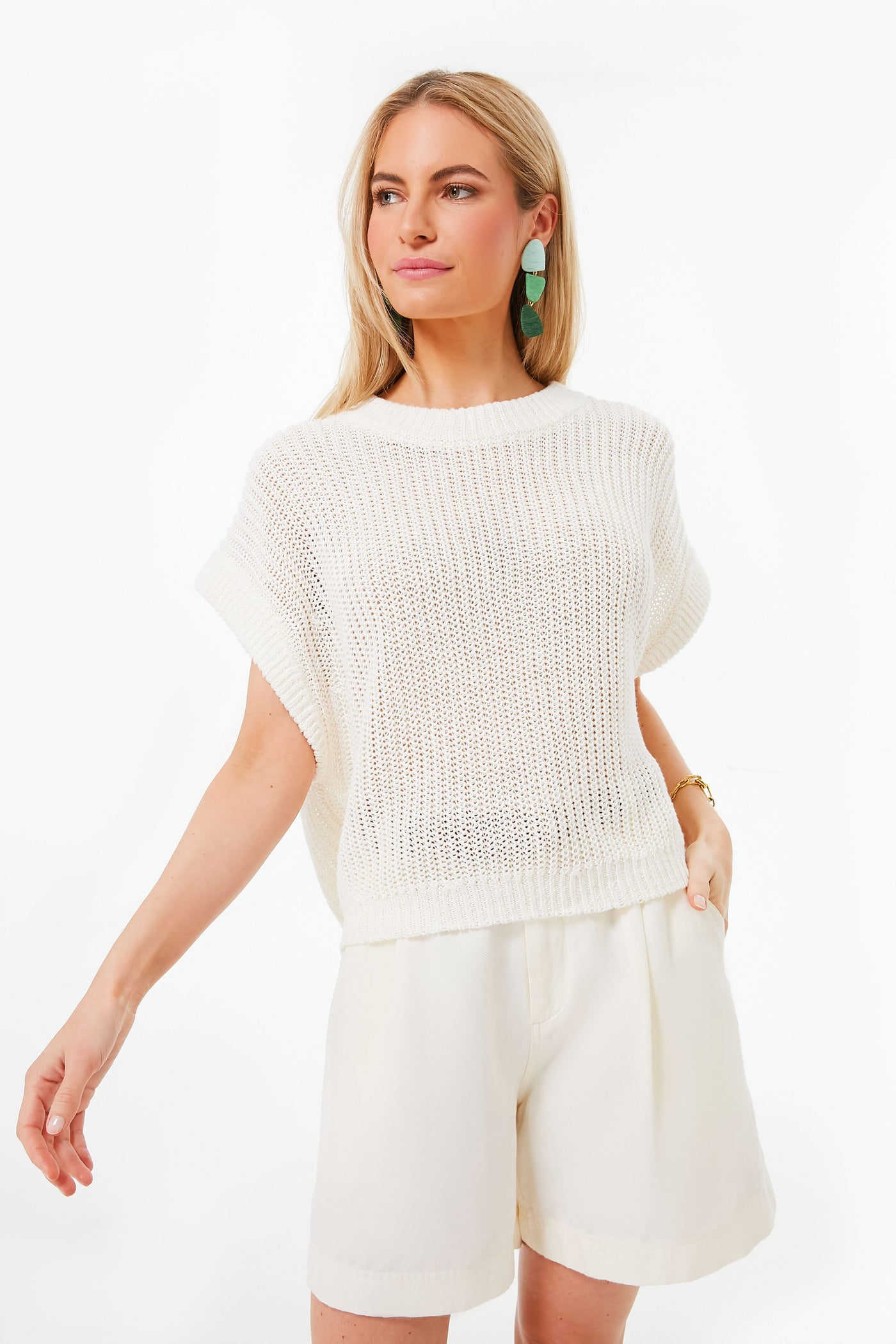 A woman wears an Apiece Apart loose-knit white short-sleeve sweater with white shorts, making it ideal for a coastal style warm-weather wardrobe.