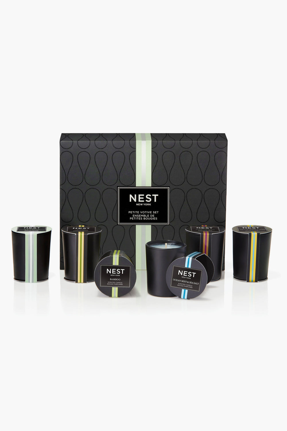A NEST New York mini votive set with six black candles in glass holders, each featuring a different colored stripe and label, displayed in front of the box.