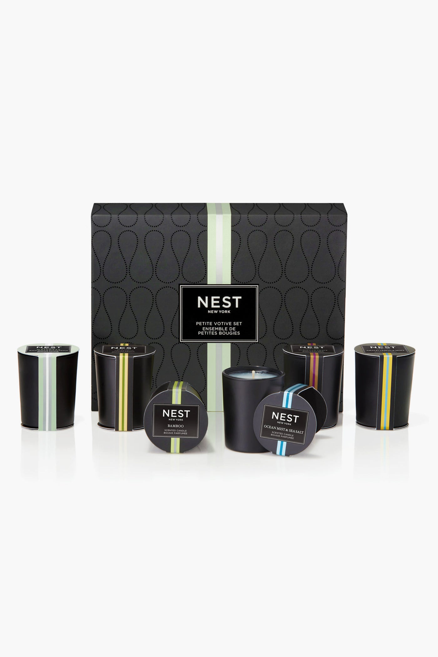 A NEST New York mini votive set with six black candles in glass holders, each featuring a different colored stripe and label, displayed in front of the box.
