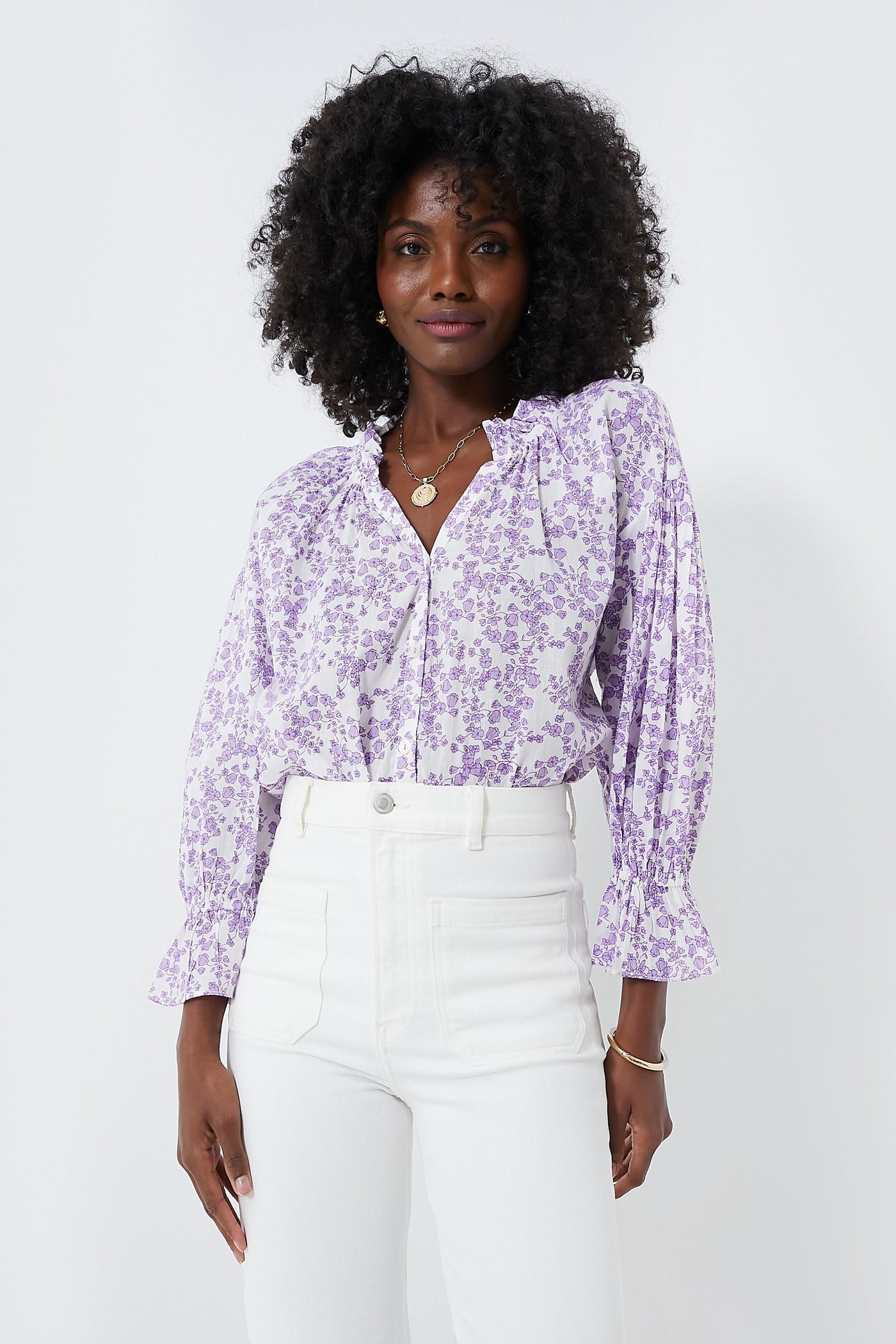 Woman wearing a lilac Ro's Garden shirt, a relaxed feminine blouse with ruffled cuffs, paired with high-waisted white pants.