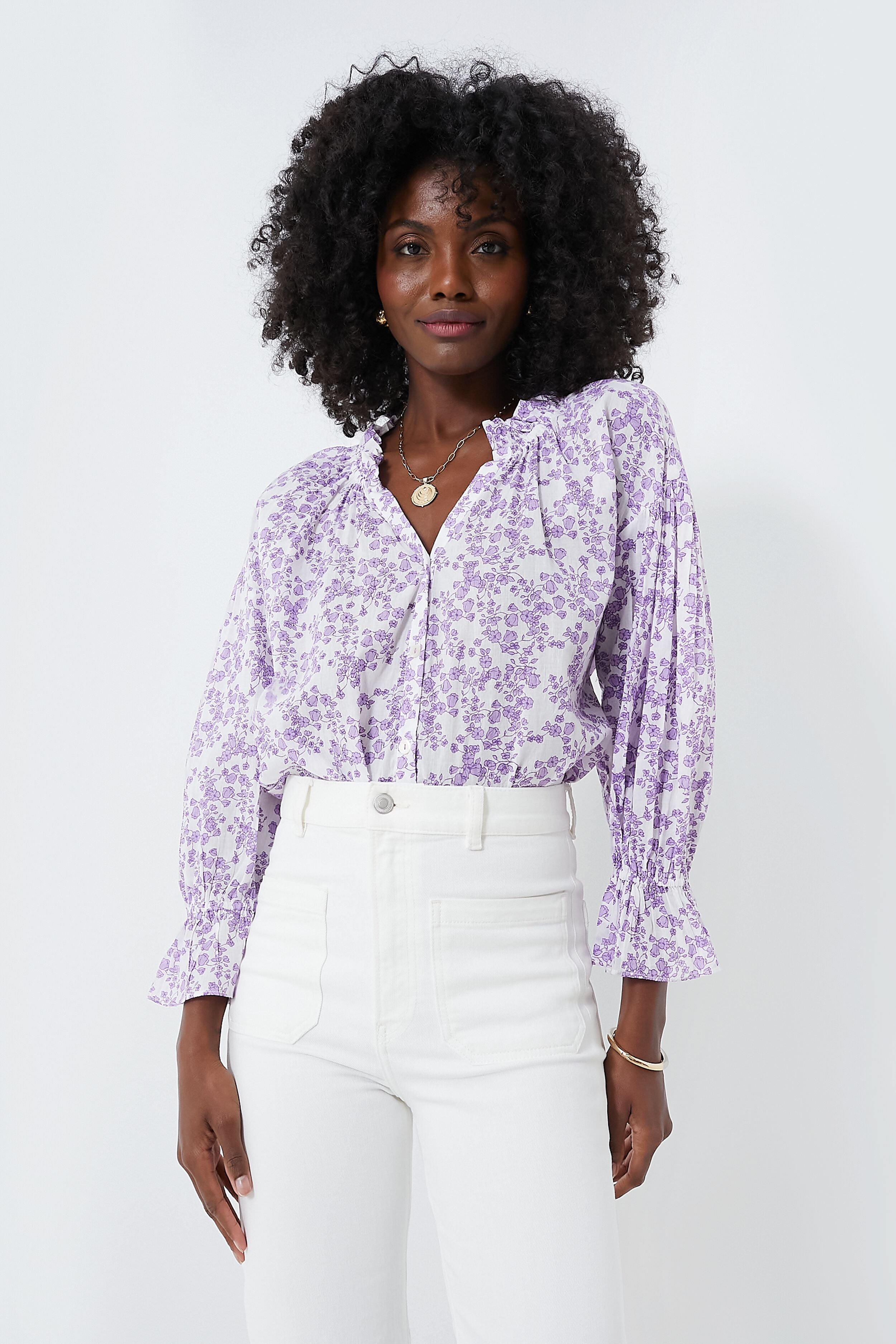 Woman wearing a lilac Ro's Garden shirt, a relaxed feminine blouse with ruffled cuffs, paired with high-waisted white pants.