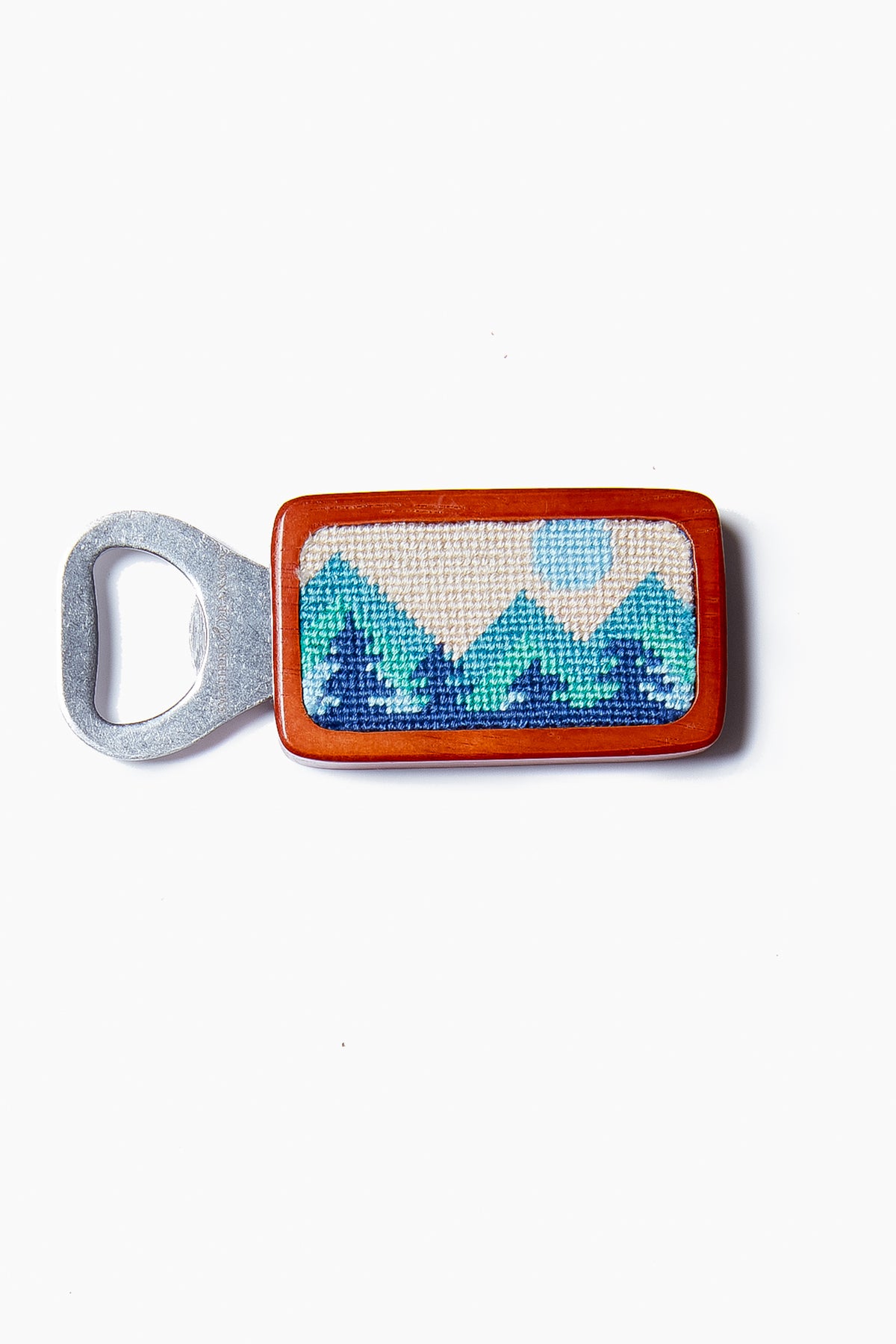 The Smathers and Branson magnetic bottle opener features a rectangular wooden handle with a hand-stitched mountain and sun design in blue and green tones.