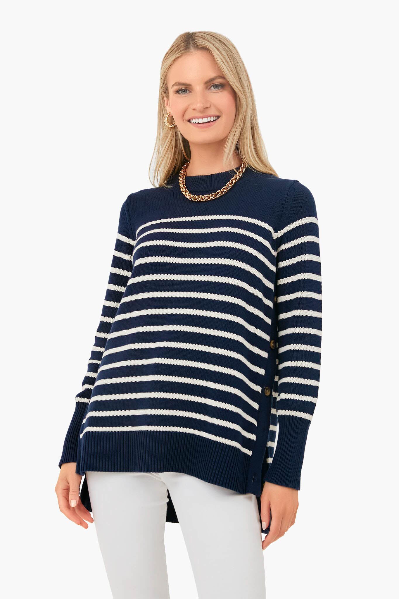 A woman smiles in a Tuckernuck navy and white striped 100% cotton sweater with side buttons and modern details, paired with white pants and a gold chain necklace.