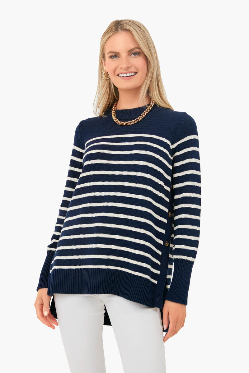 A woman smiles in a Tuckernuck navy and white striped 100% cotton sweater with side buttons and modern details, paired with white pants and a gold chain necklace.