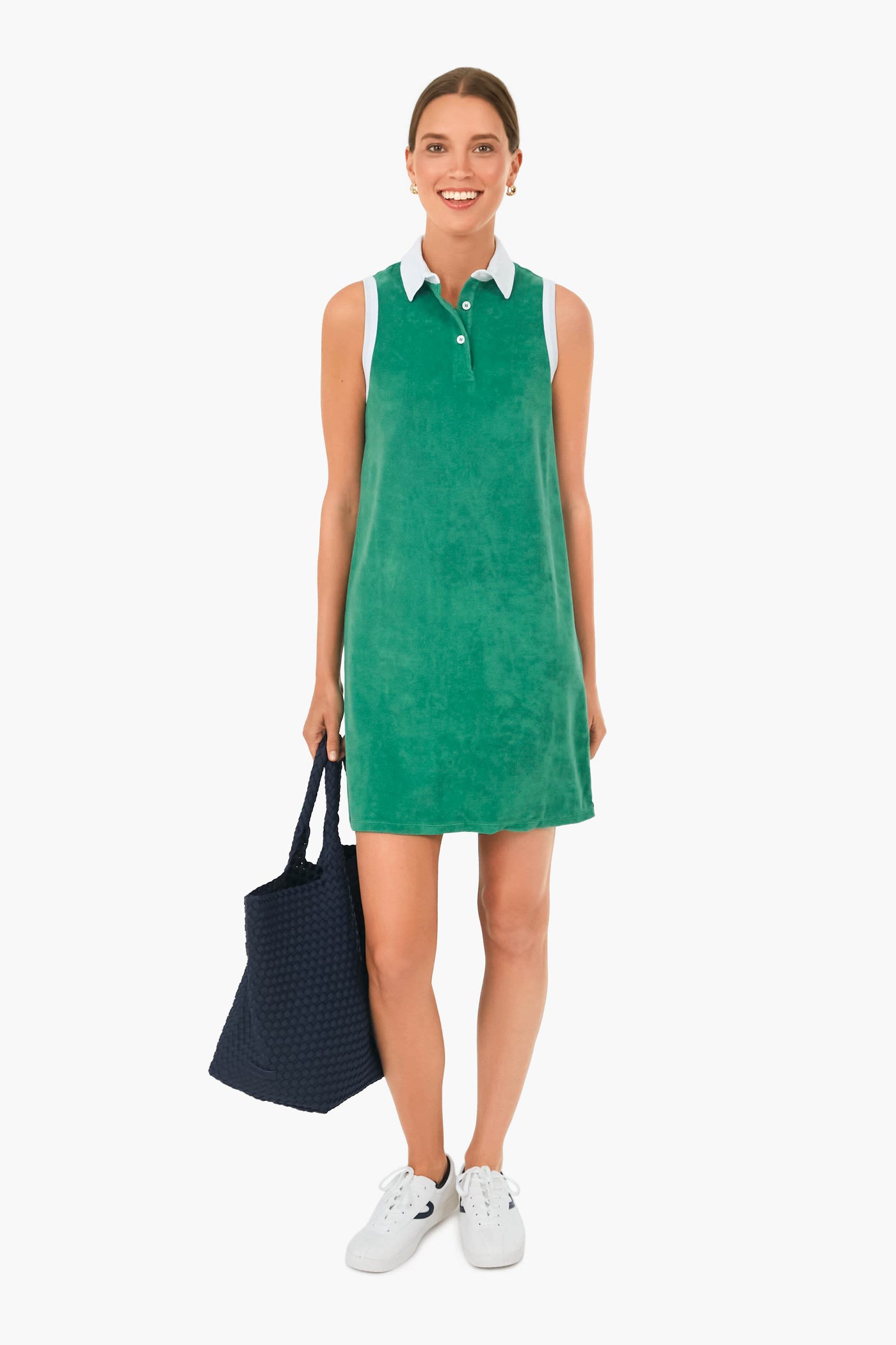 A woman wears a sleeveless green KULE polo dress with a white collar, paired with white sneakers, and carries a navy blue tote bag.